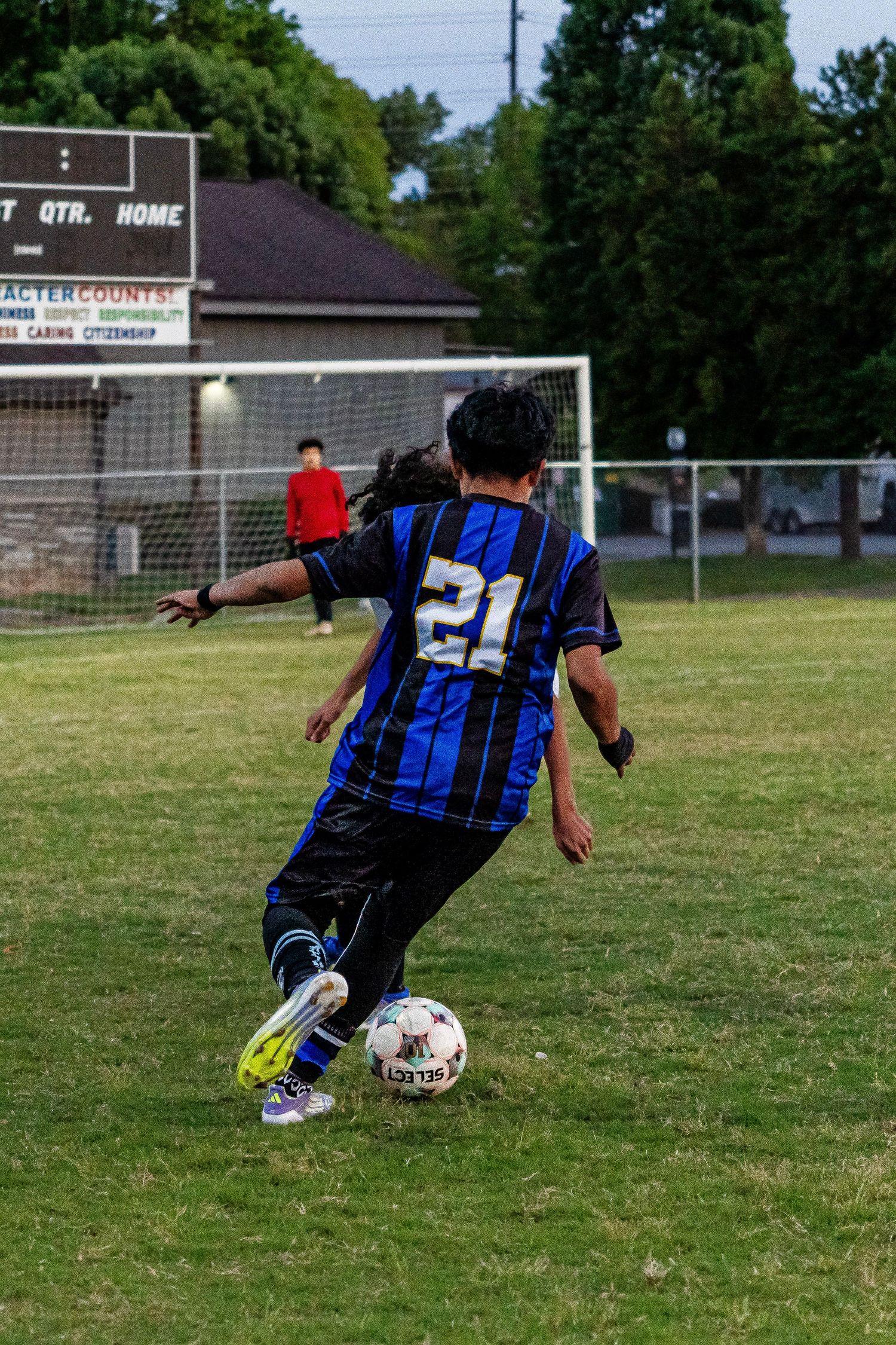 Soccer player #21 in blue and black jersey dribbles ball toward goal during outdoor match.