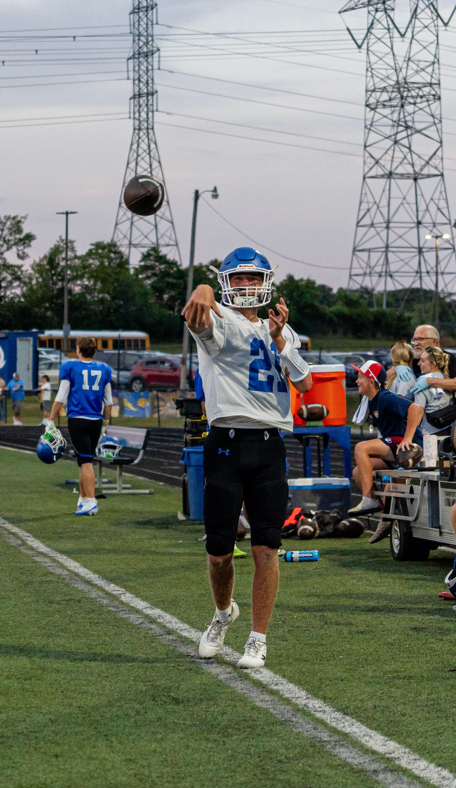 Youth football quarterback #21 in blue helmet throws pass on sideline during warm-ups.