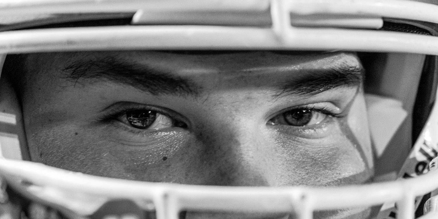 Close-up black and white shot of a football player's eyes through a helmet face mask.