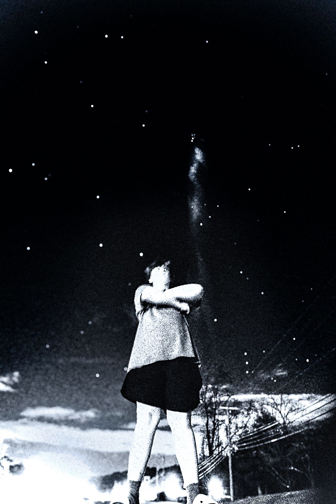 Black and white photo of a person standing under a starry night sky with arms crossed, smoke rising above them.