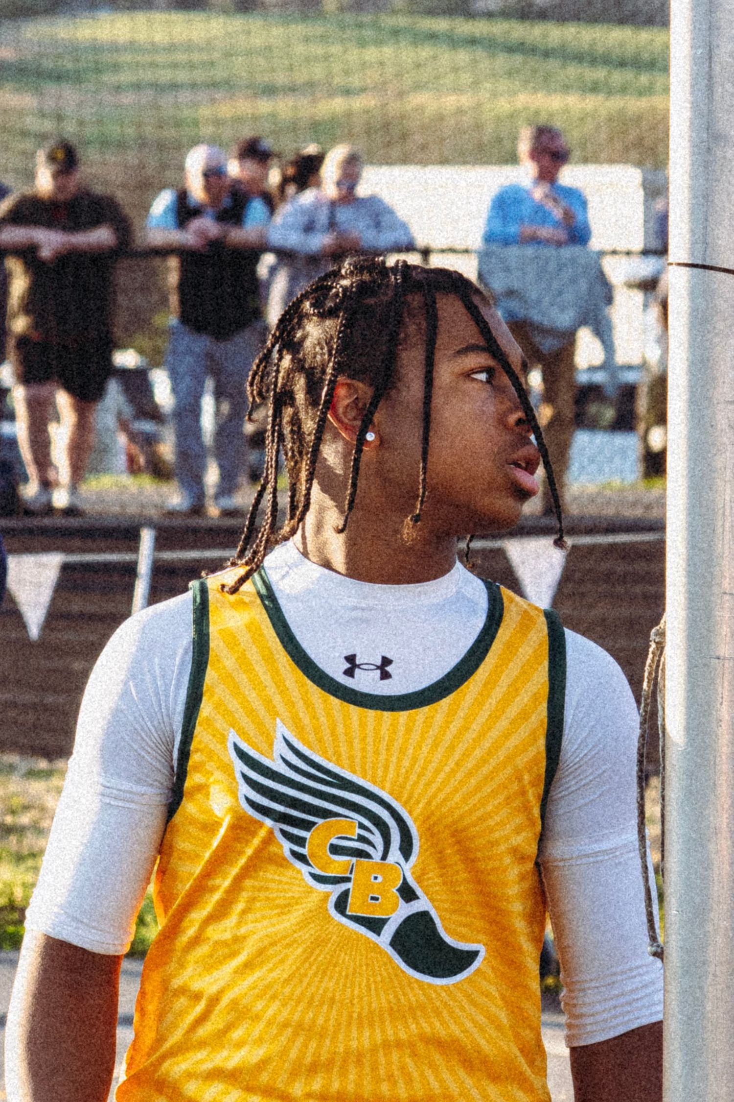 Young male track athlete in yellow CB jersey with braids stands at outdoor competition.