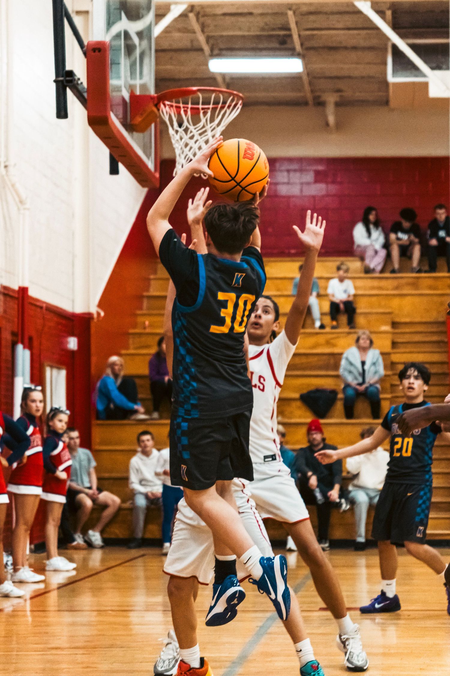 A basketball player in a dark number 30 jersey drives to the hoop against defenders in a gym.