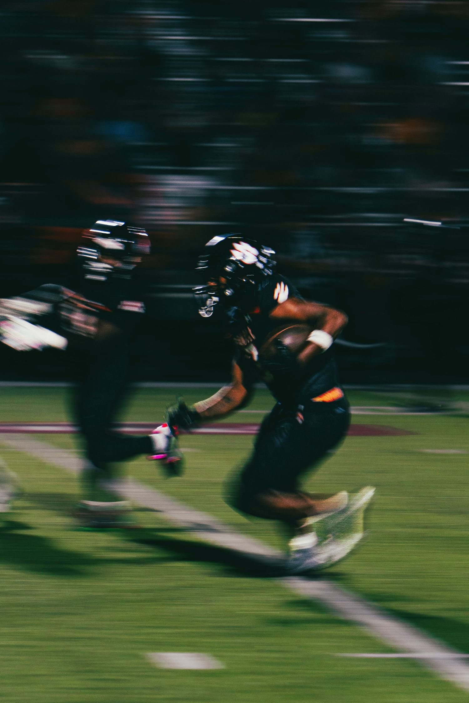 Motion blur action shot of football players in dark uniforms running with the ball during a game.