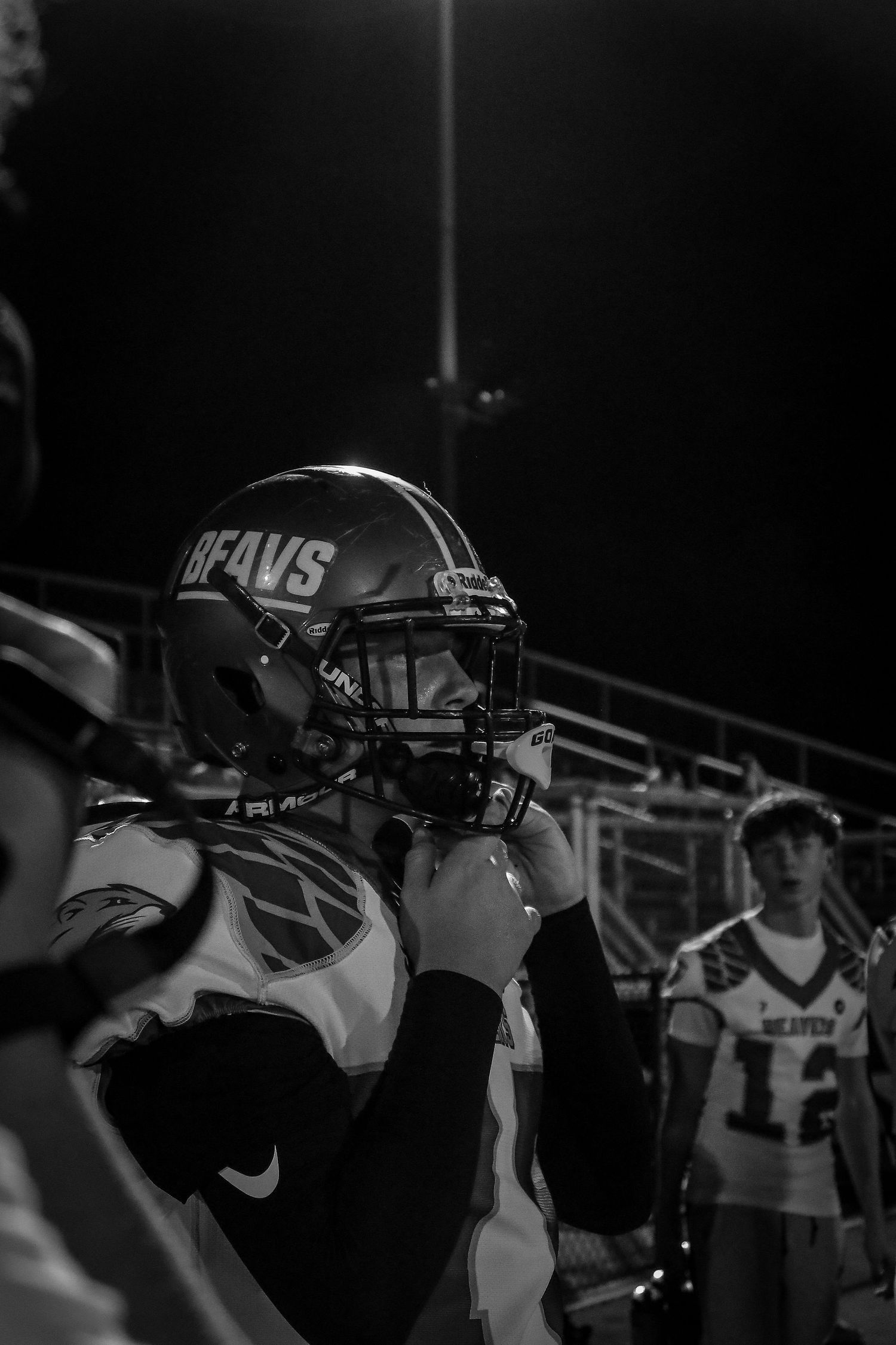 Black and white photo of a football player in a Beavs helmet adjusting his gear on the sideline.