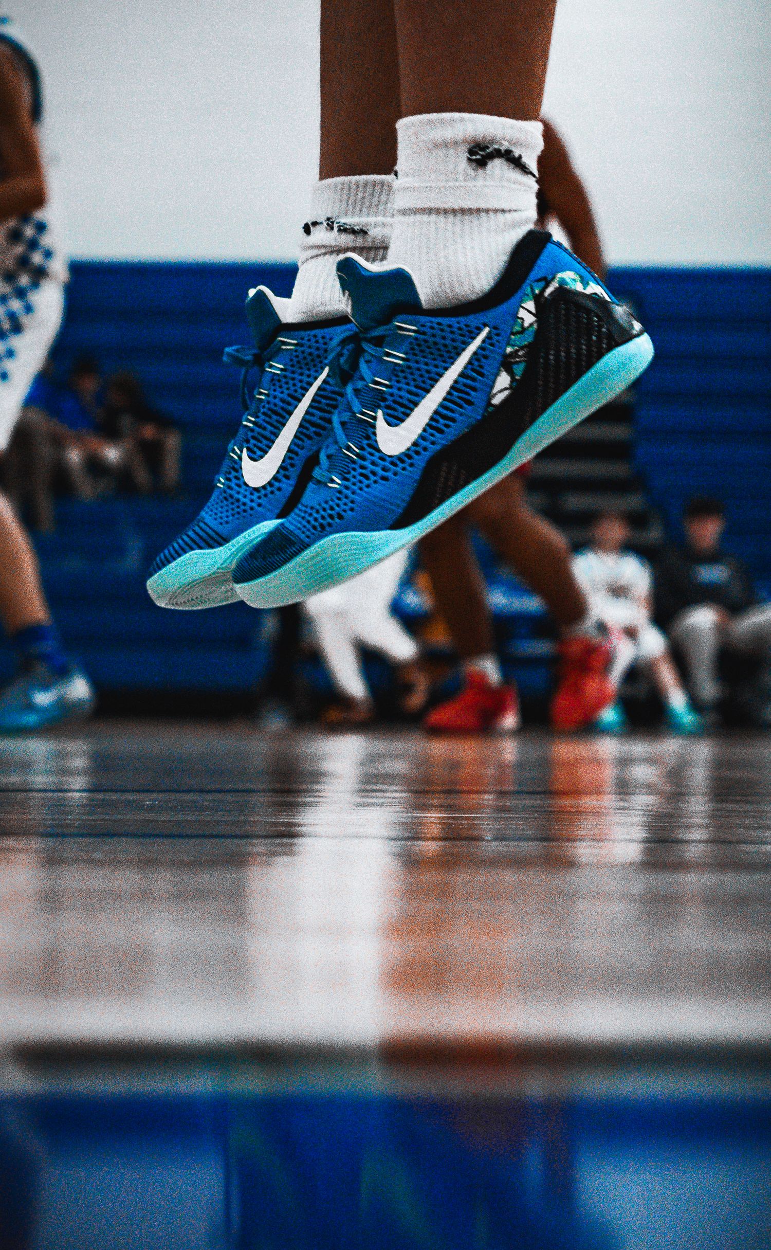 Close-up of blue Nike basketball shoes mid-jump reflecting on hardwood court during indoor game.