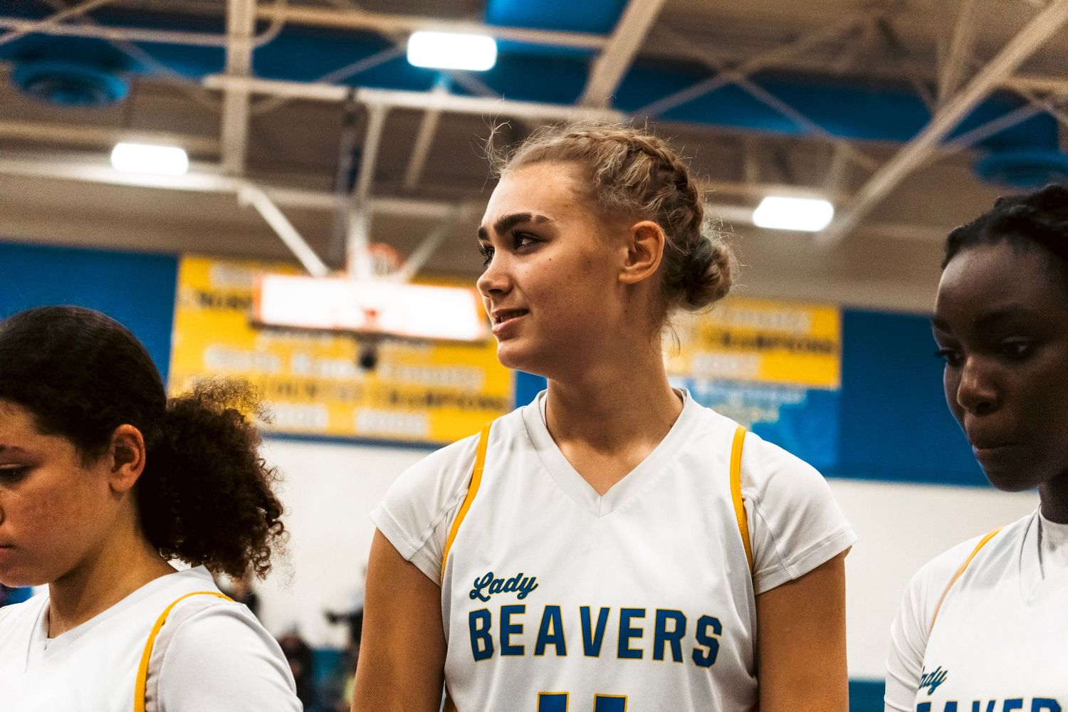 Lady Beavers player #11 with braided hair stands among teammates during a basketball game.