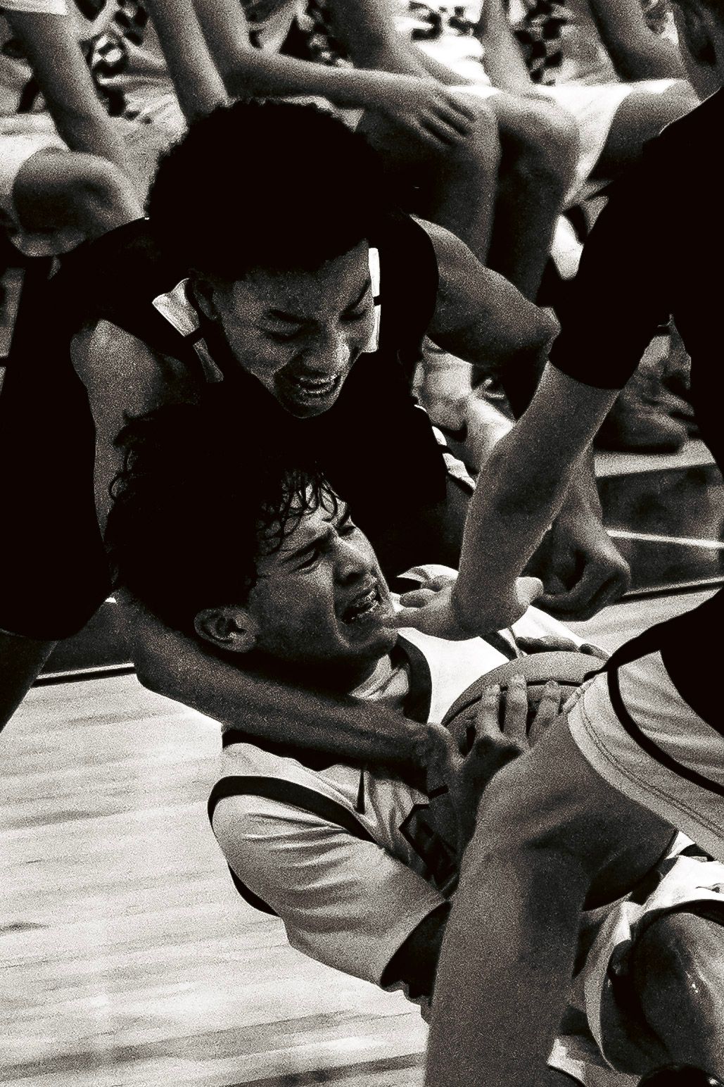 Two basketball players scramble intensely on the court floor in a dramatic black and white action photo.