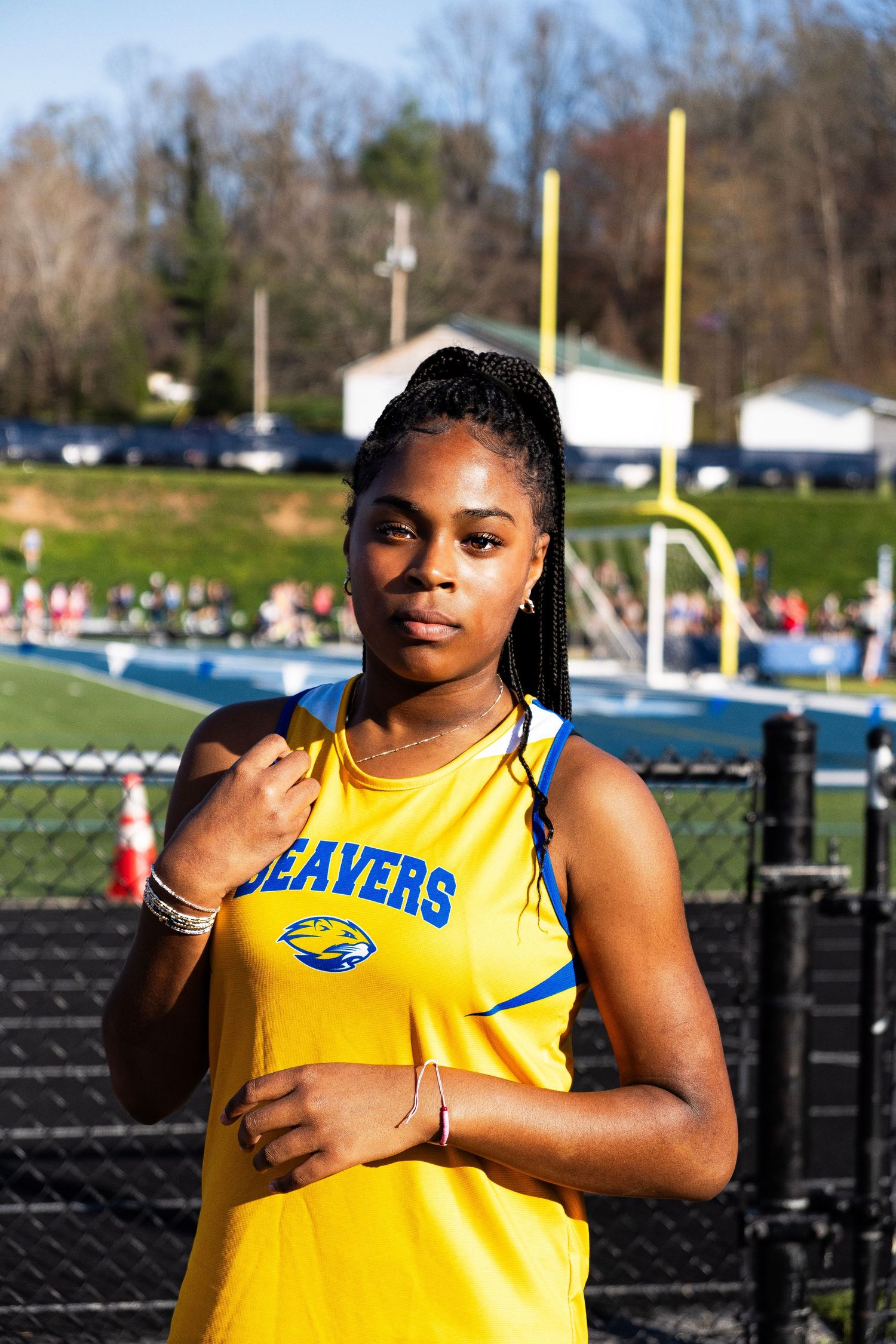 A focused female Beavers track athlete in yellow uniform poses confidently at an outdoor stadium.