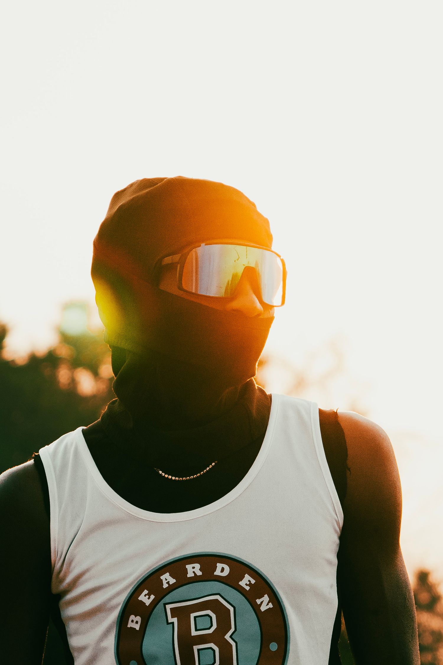 Athlete wearing a balaclava and reflective goggles backlit by golden sunset light in a Bearden tank top.