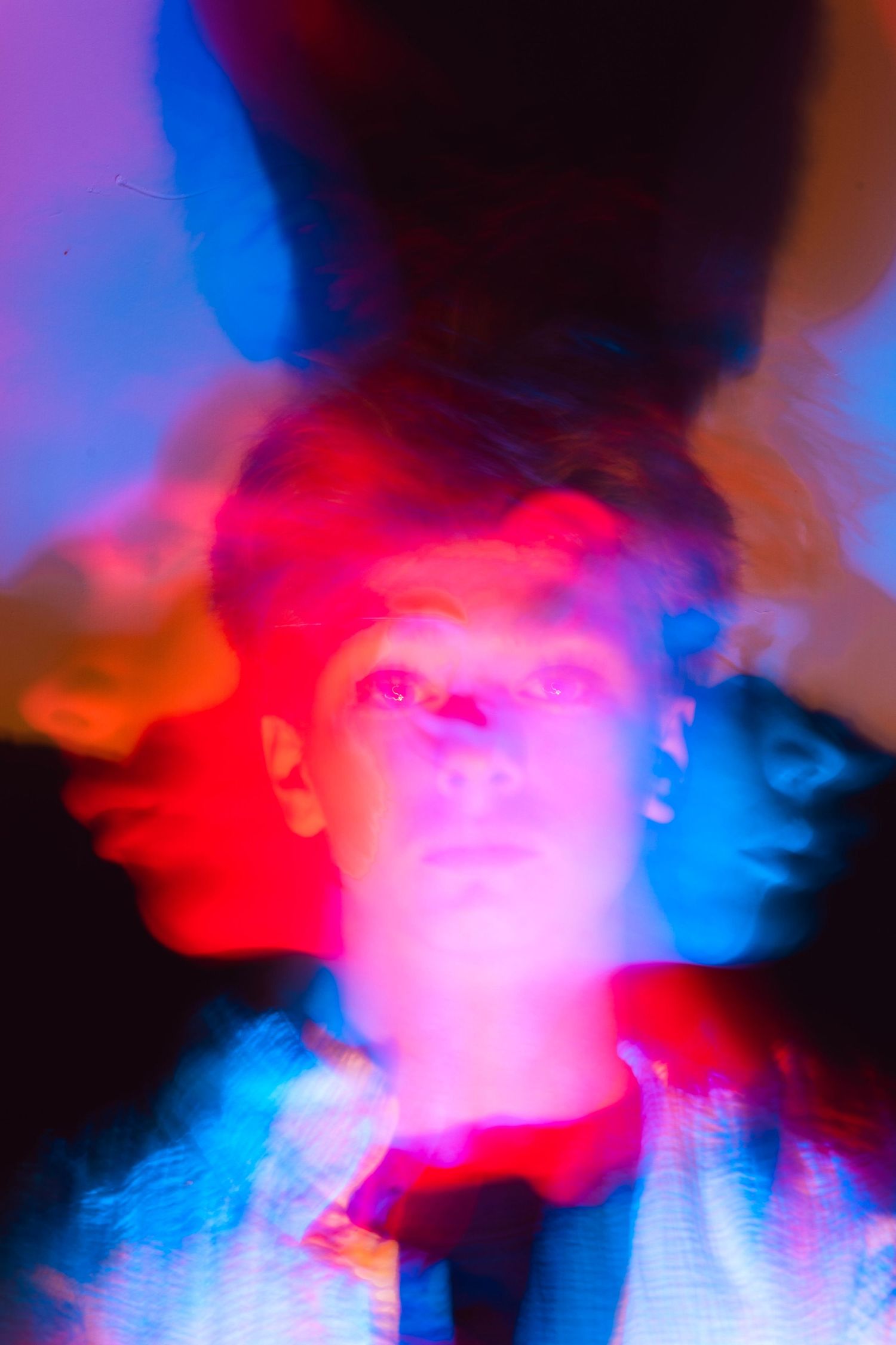 Abstract long exposure portrait of a person illuminated by red and blue colored lights.