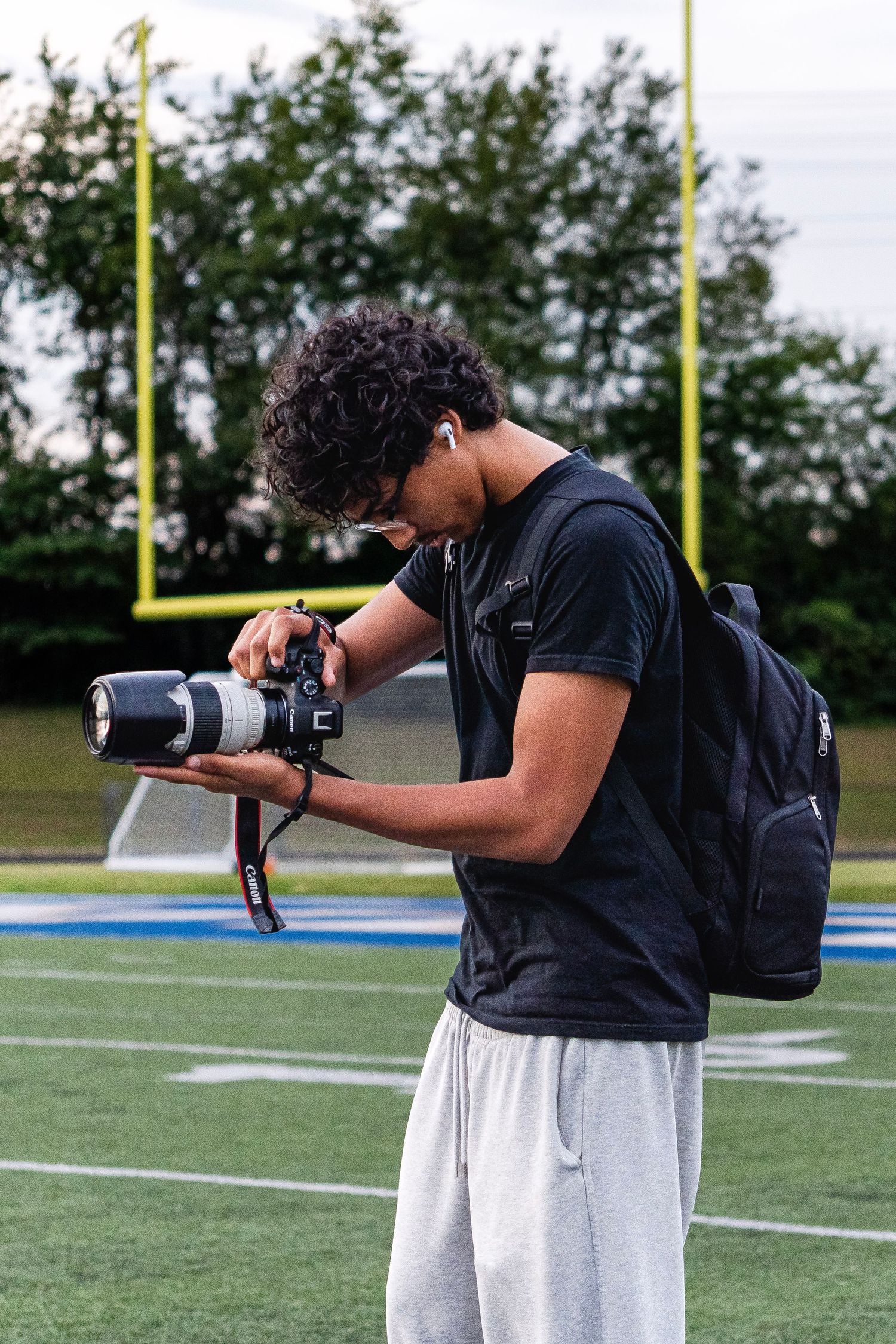 Young photographer reviewing photos on DSLR camera with telephoto lens on a football field.