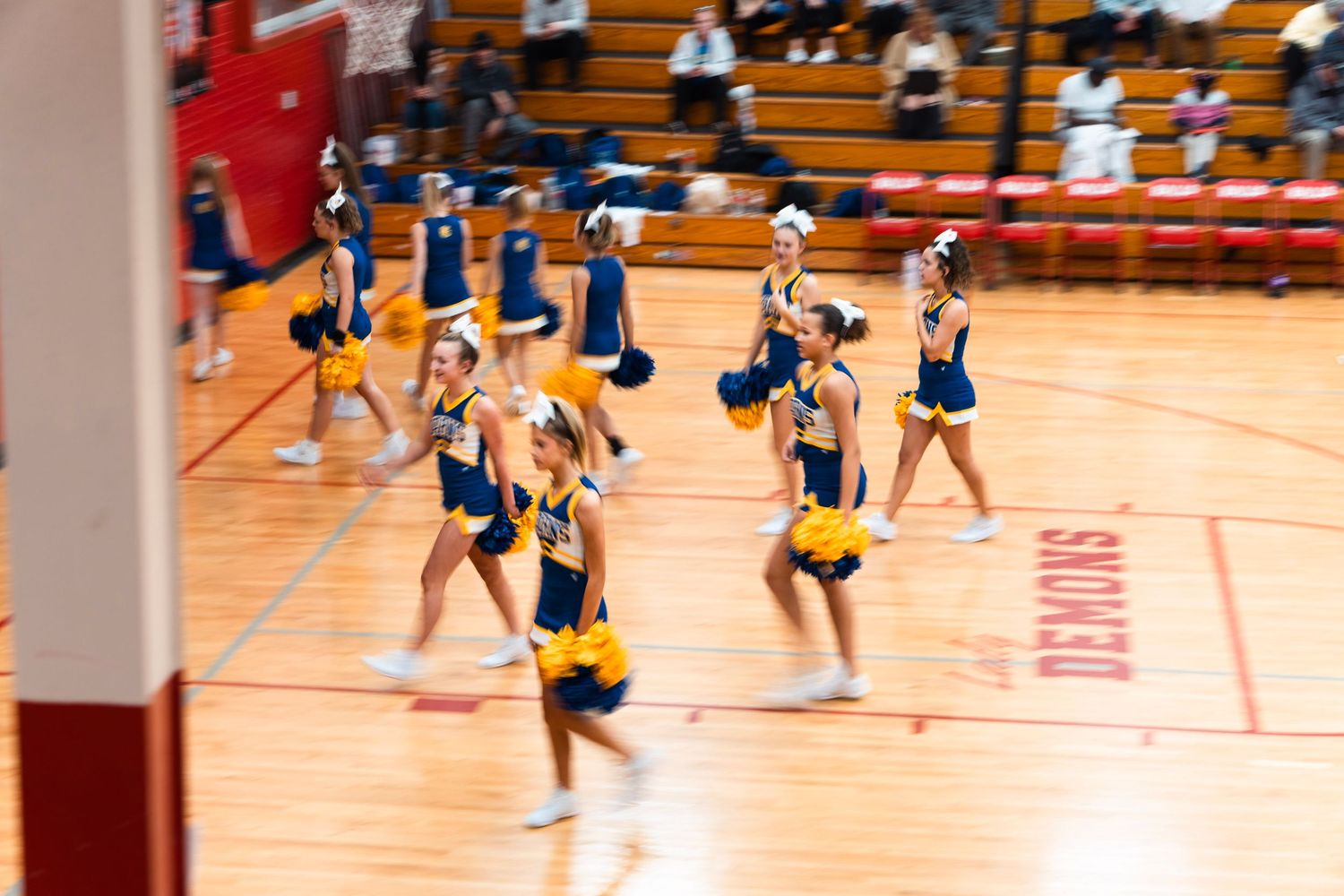 Middle school cheerleading squad performing a routine in yellow and blue uniforms in a red gymnasium.