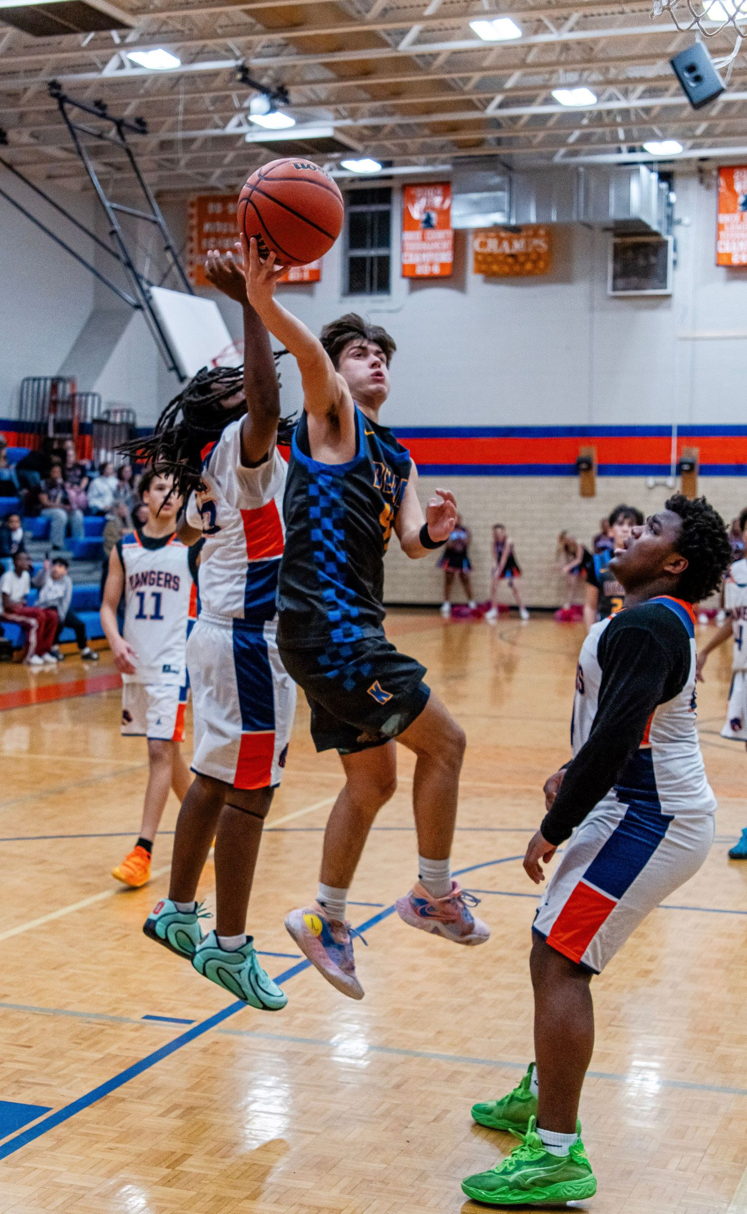 A youth basketball player in a checkered jersey leaps for a layup during an indoor basketball game.