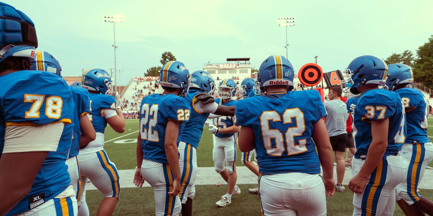 Football team in blue and gold uniforms gathered on field before game.