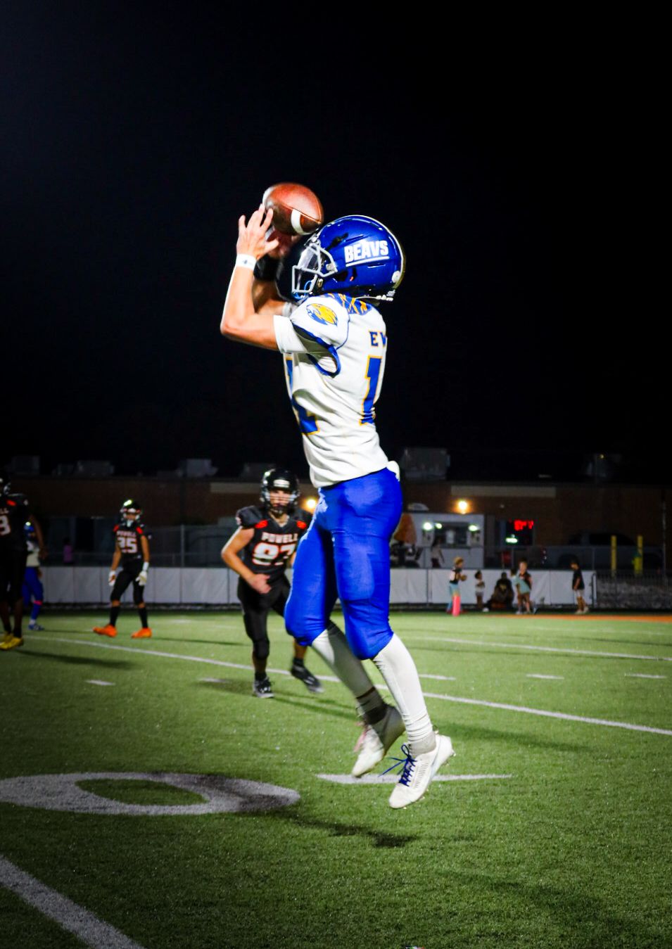 A football player in blue uniform leaps to catch a pass during a night game.