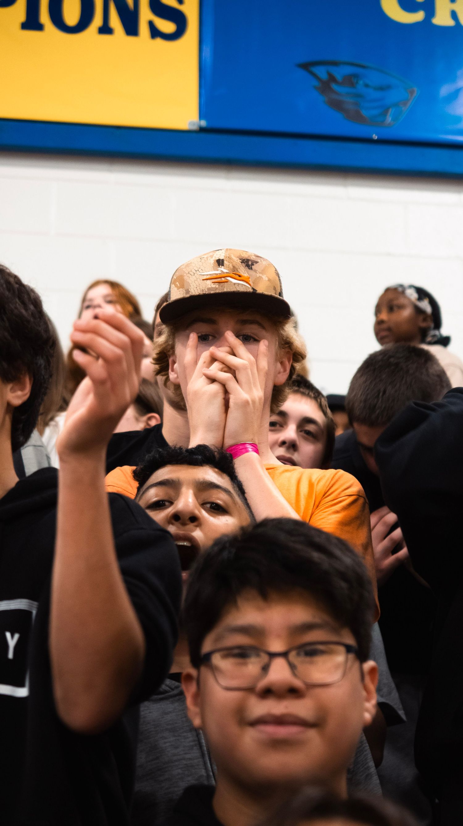 Excited student fans crowd together in bleachers cheering at a school basketball game.