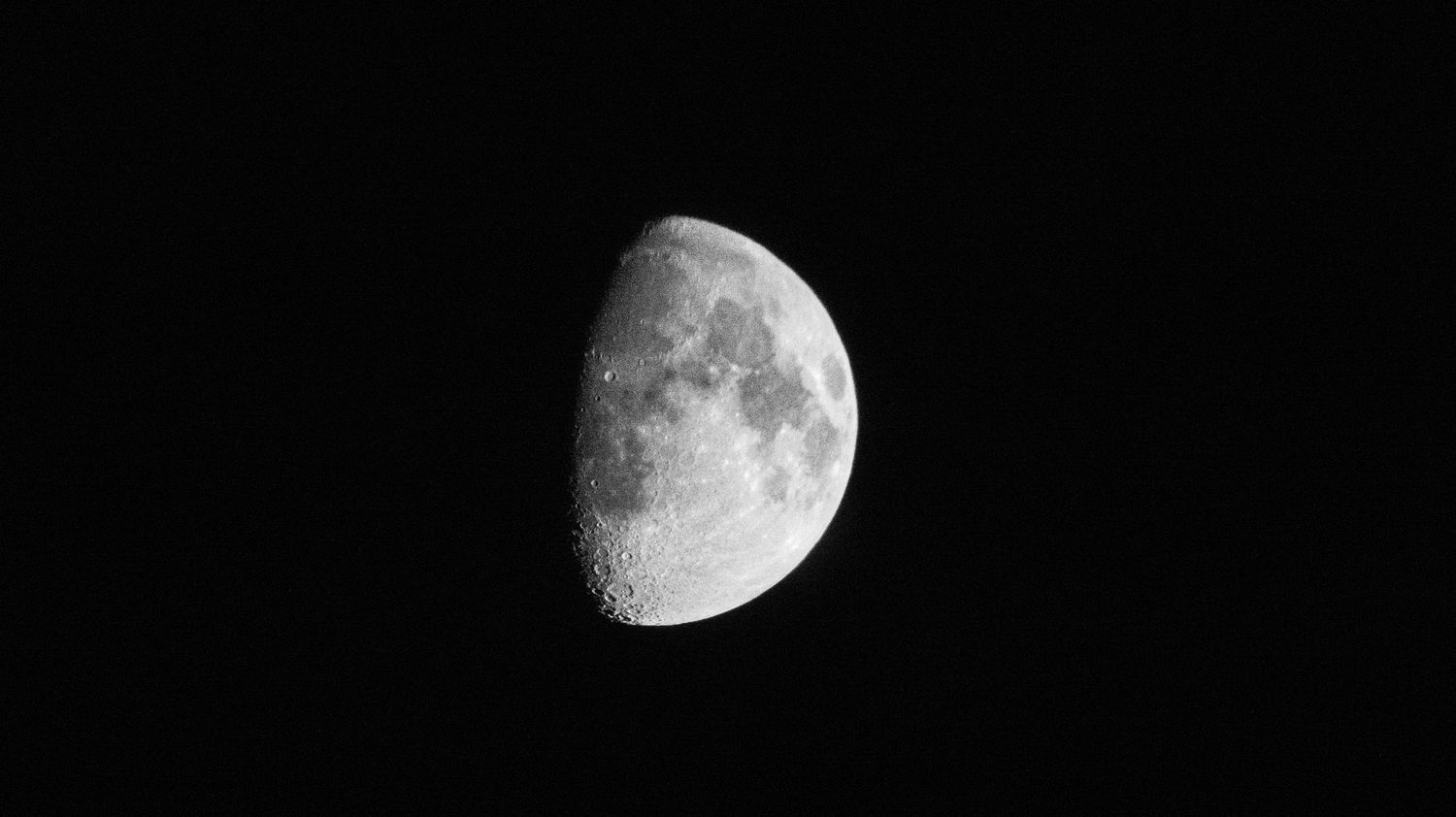 A detailed close-up photograph of a half moon against a dark black night sky.