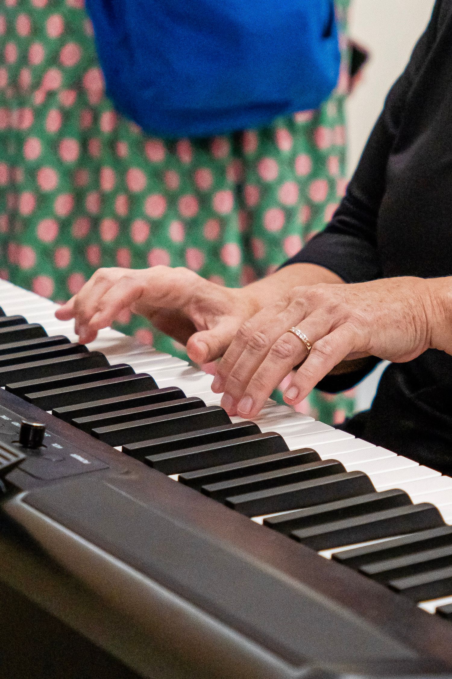Elderly hands with a gold ring playing keys on a digital piano keyboard.