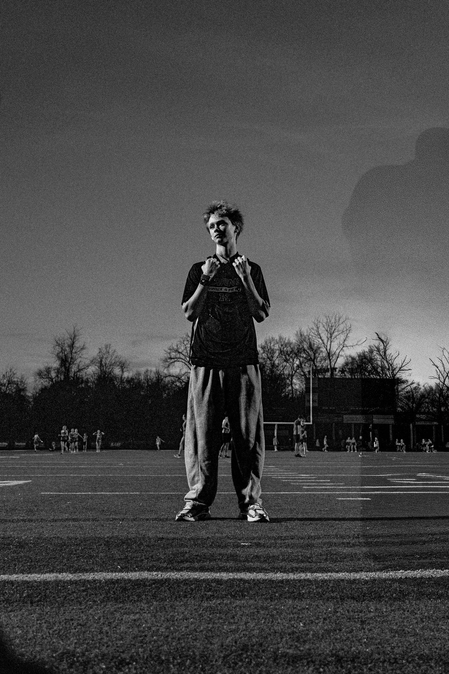 A young male track athlete stands confidently on a field in black and white photography at dusk.