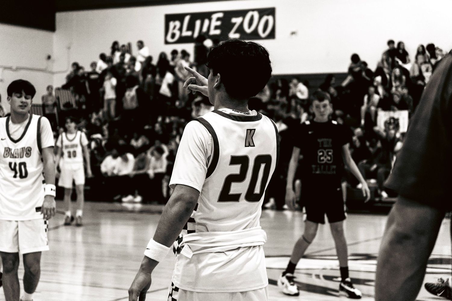 Basketball player wearing number 20 jersey on court with Blue Zoo sign and packed crowd visible in background.