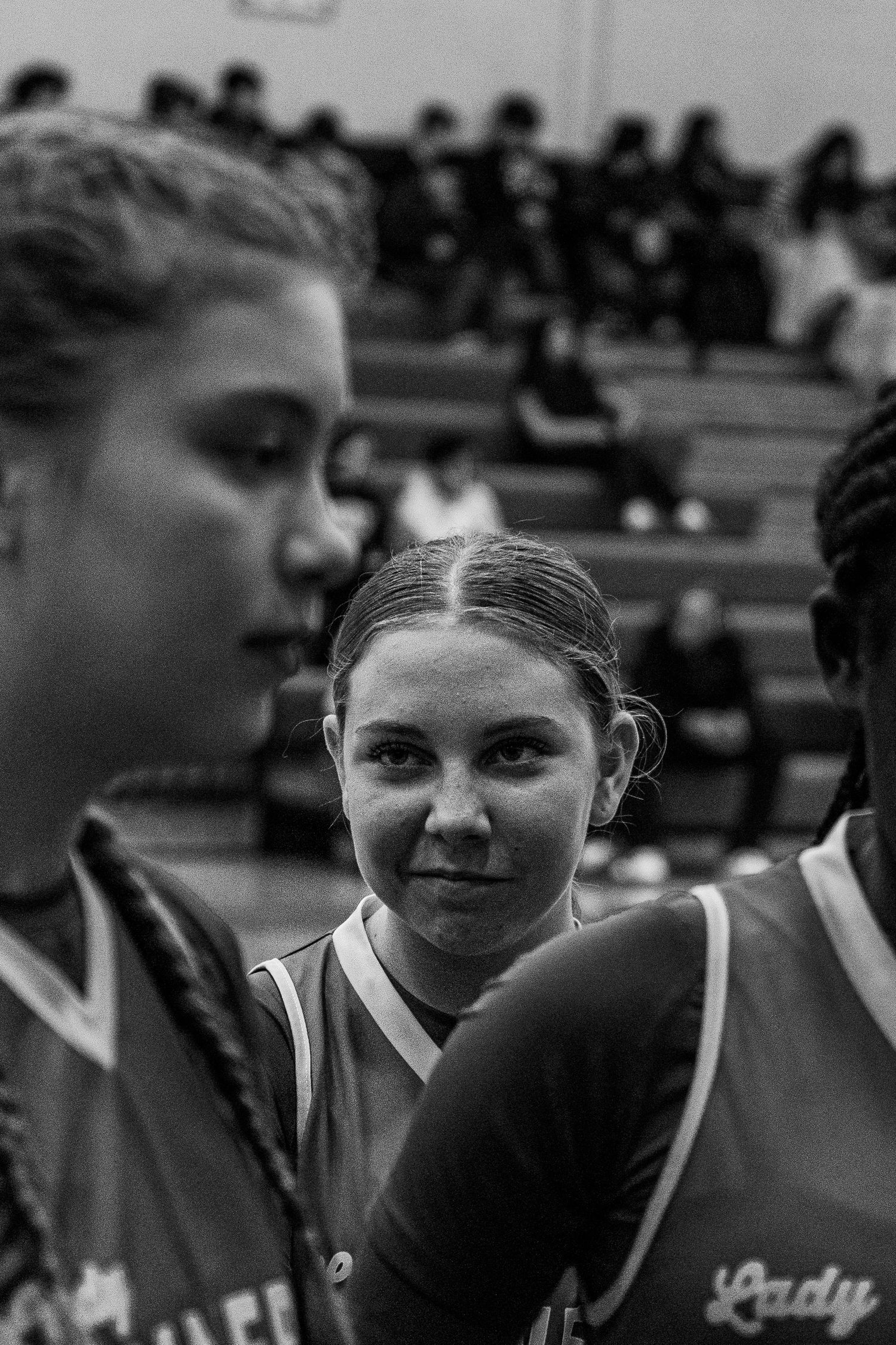 Black and white photo of female basketball players in Lady uniform huddling during high school game.