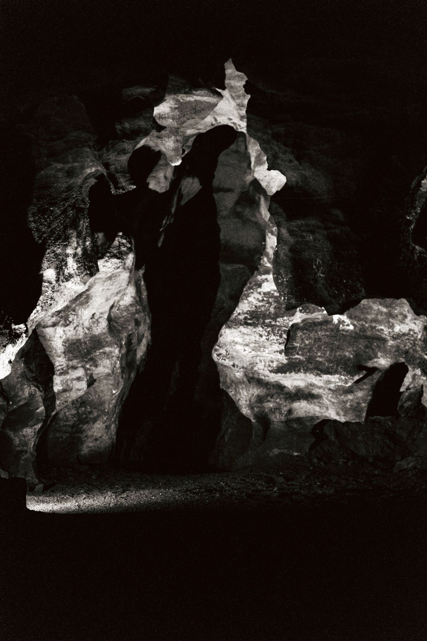Black and white photo of dramatic cave rock formations with light filtering through crevices.