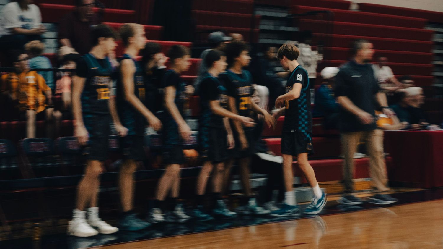 A high school basketball team in dark teal uniforms walks along the sideline during a game.