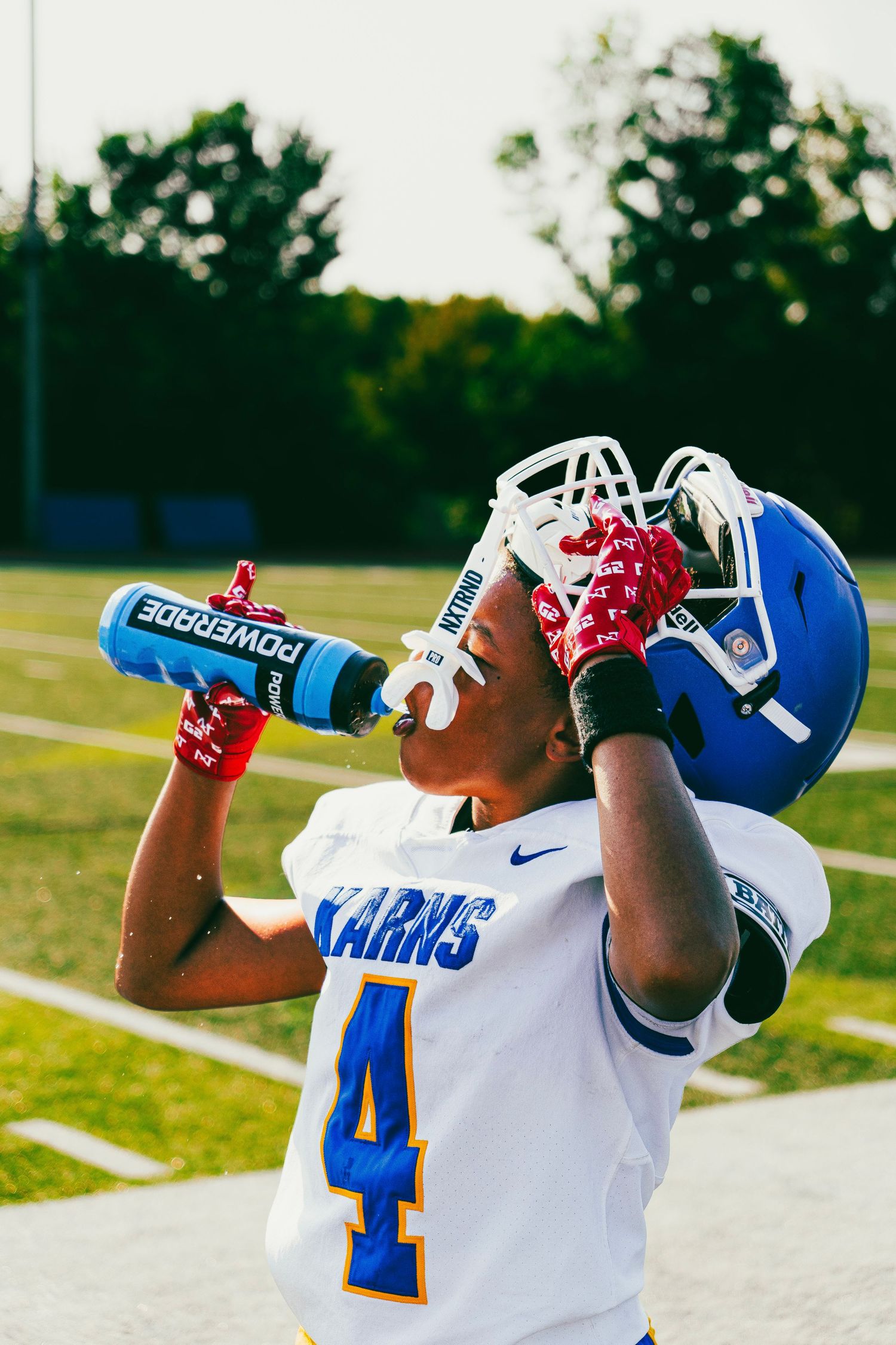 Karns football player number 4 drinking Powerade while lifting his blue helmet on the field.