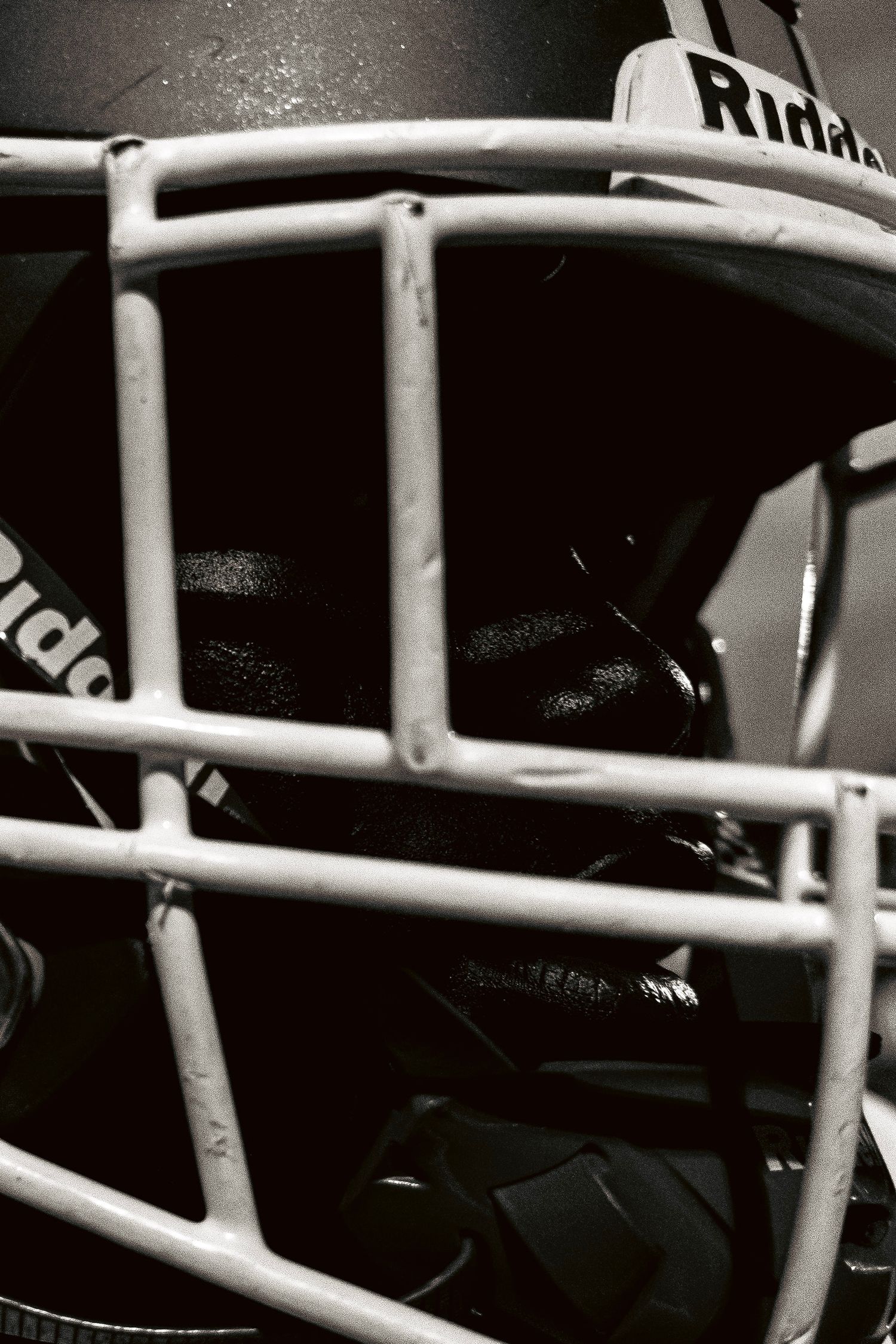 Black and white close-up of a Riddell football helmet face mask with dramatic lighting.