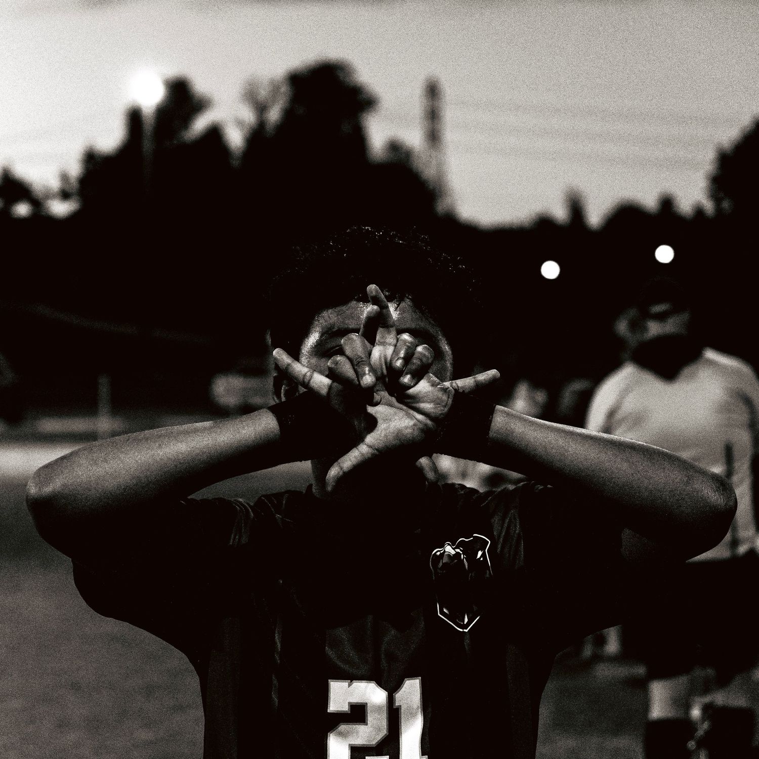 Black and white photo of soccer player #21 covering face with hands on dark field.