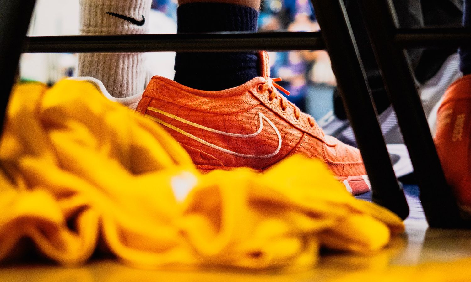 Close-up of an orange Nike sneaker resting on yellow fabric at a basketball game.