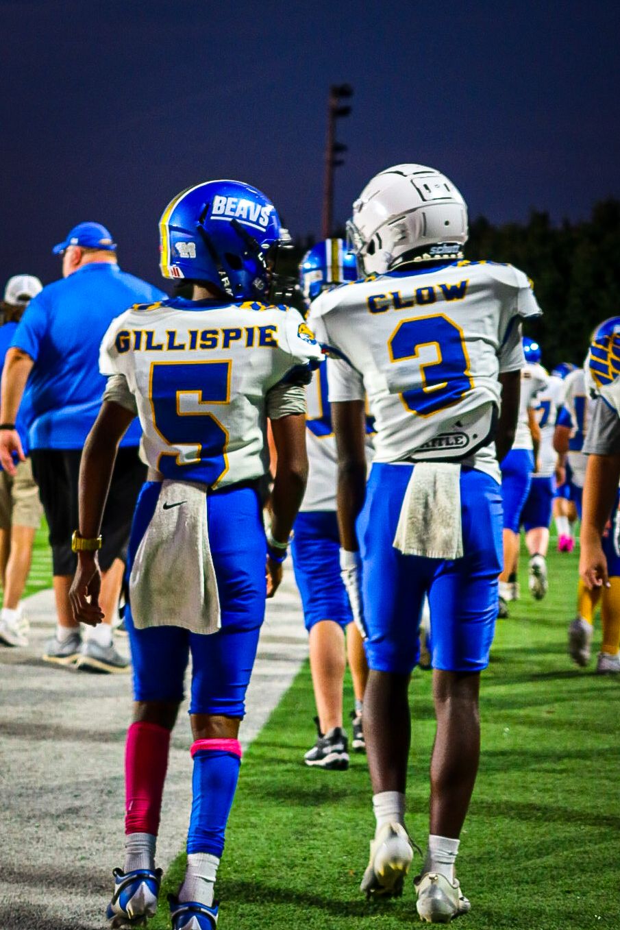Beavs football players Gillispie #5 and Clow #3 walk the sideline together in blue and white uniforms at night.