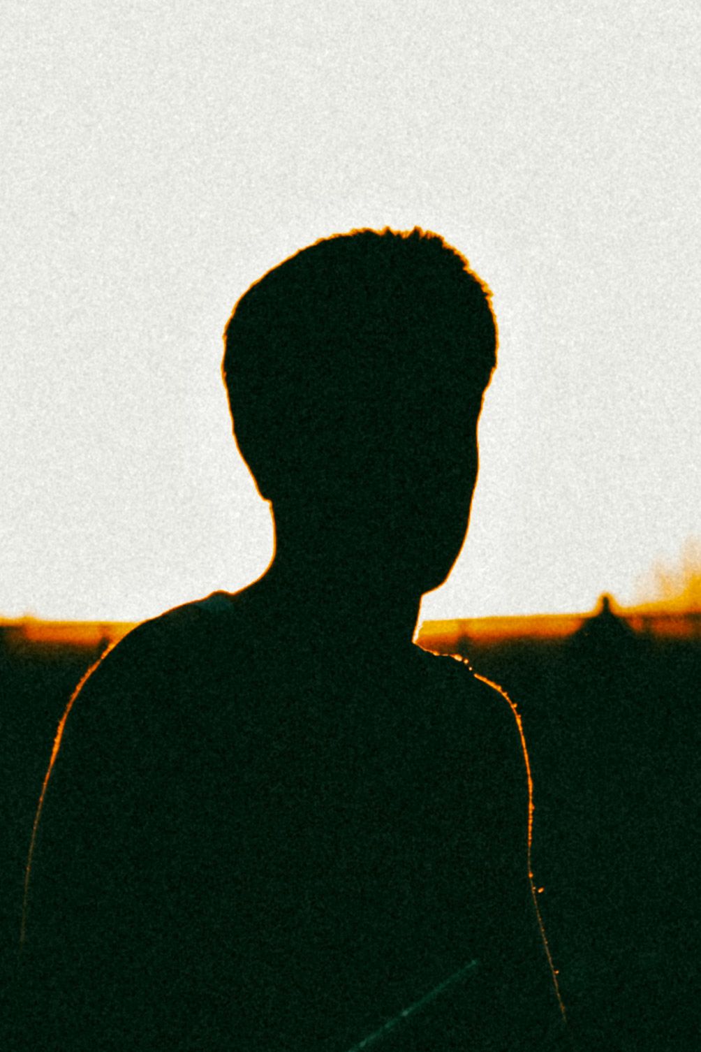 Dark silhouette of a person against a warm golden sunset background with film grain.