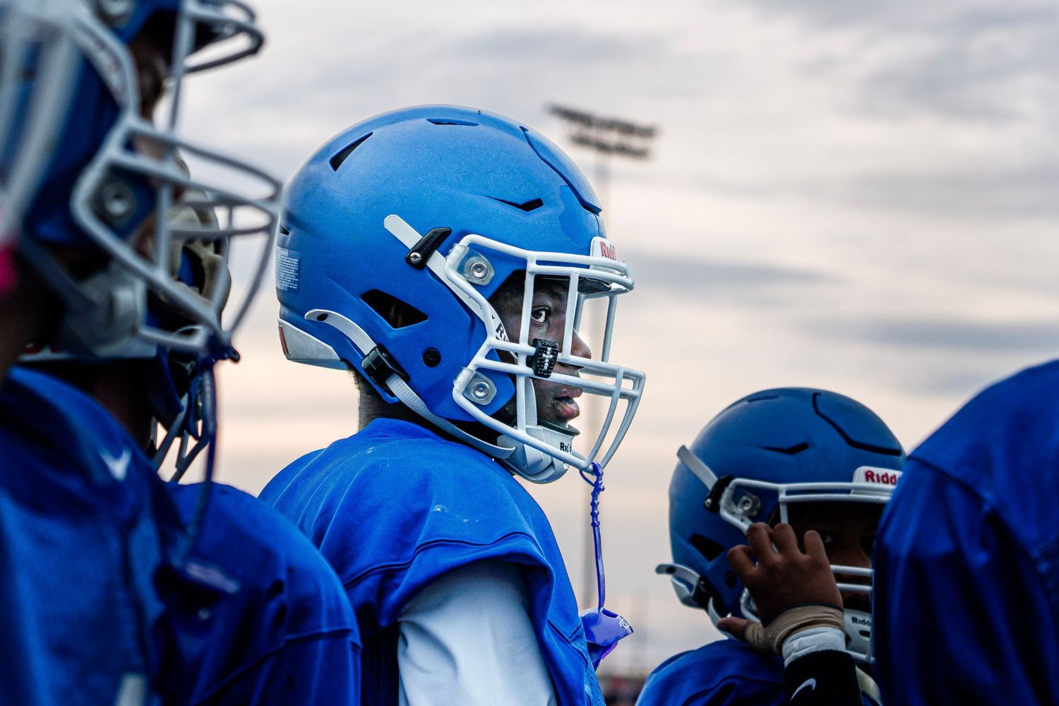 Group of football players in blue helmets and uniforms gathered on field.