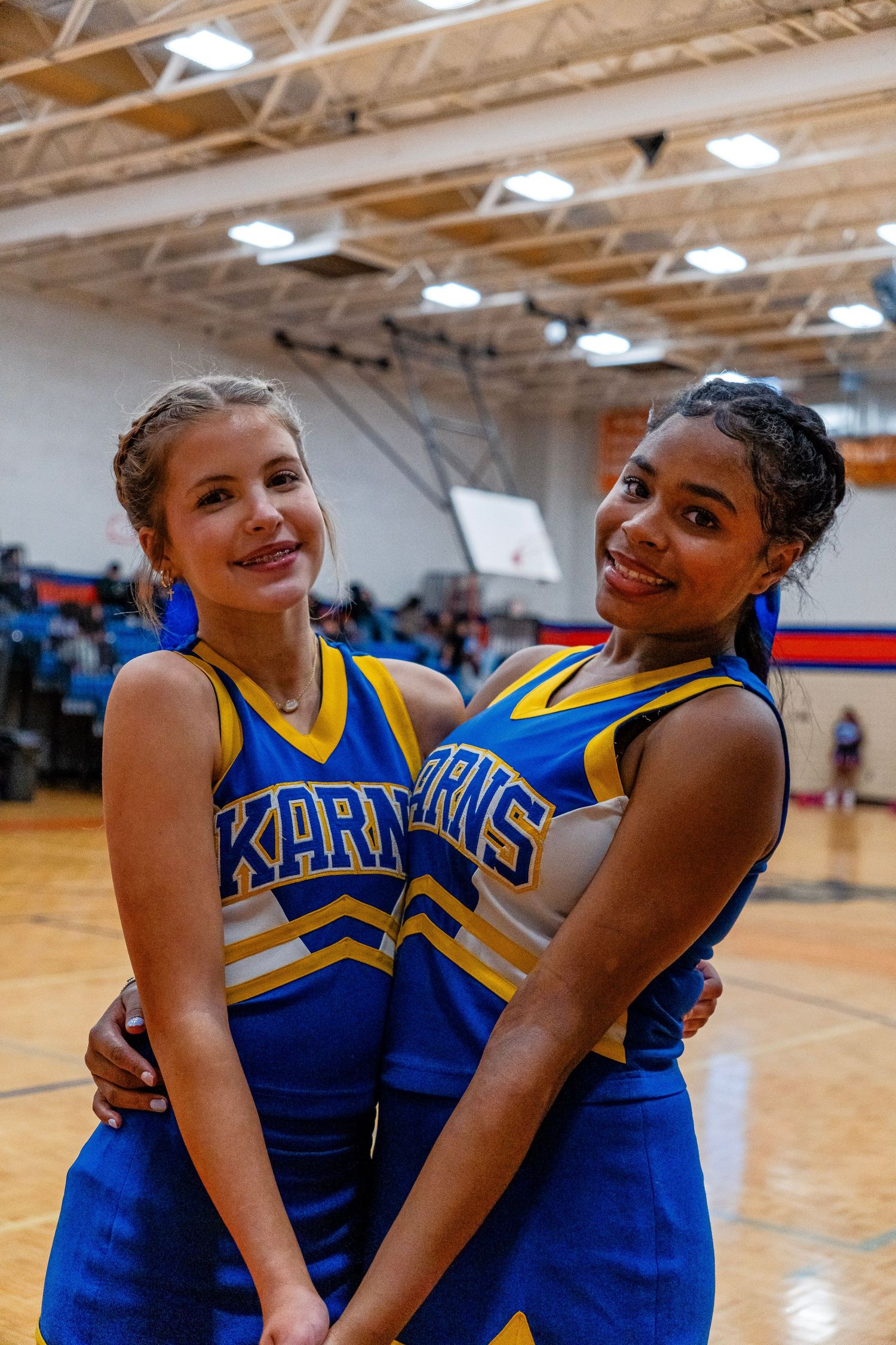 Two Karns cheerleaders smile and pose together on a school gymnasium floor.