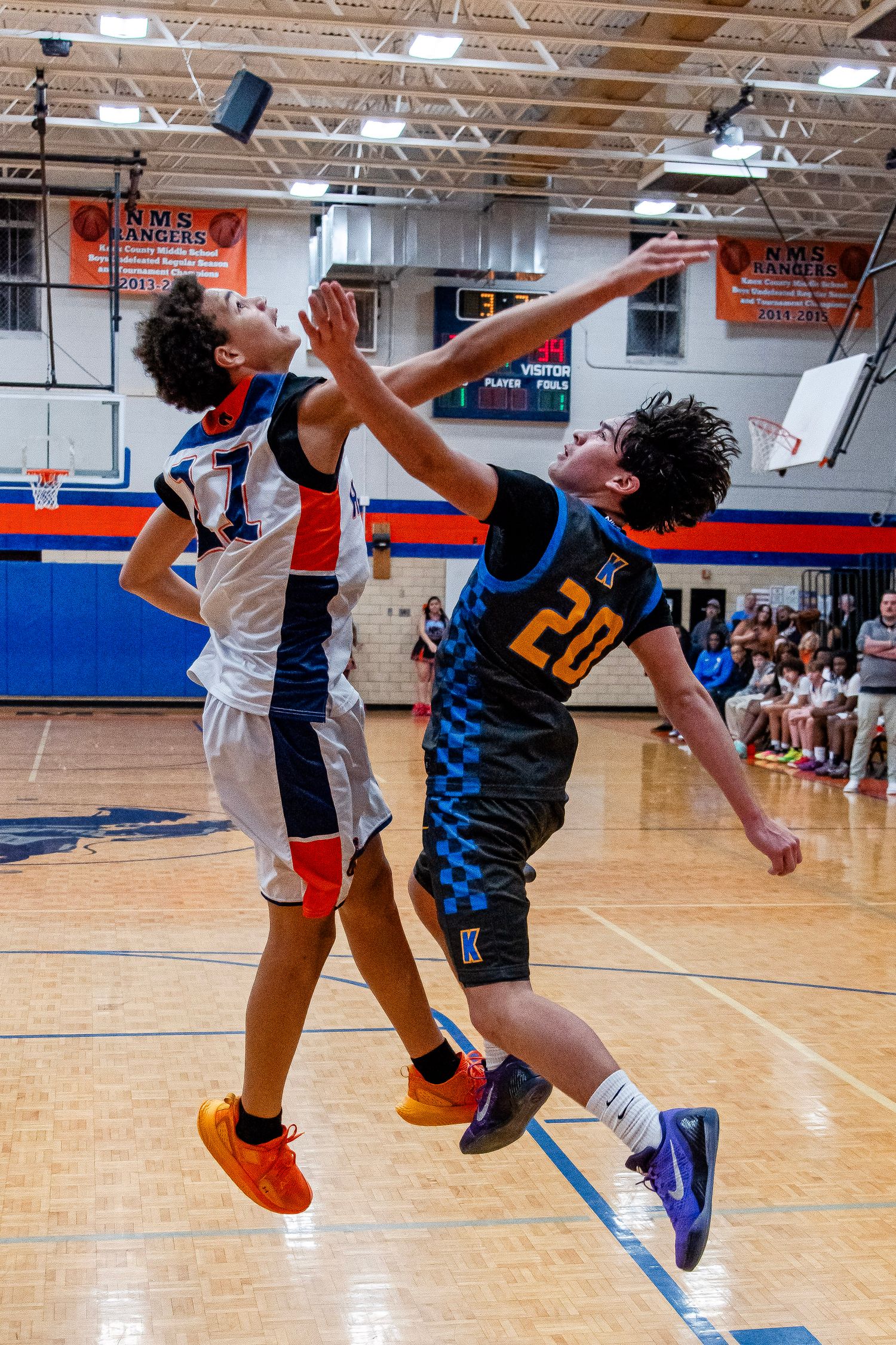 Two youth basketball players jump for the ball during an intense game in a school gymnasium.