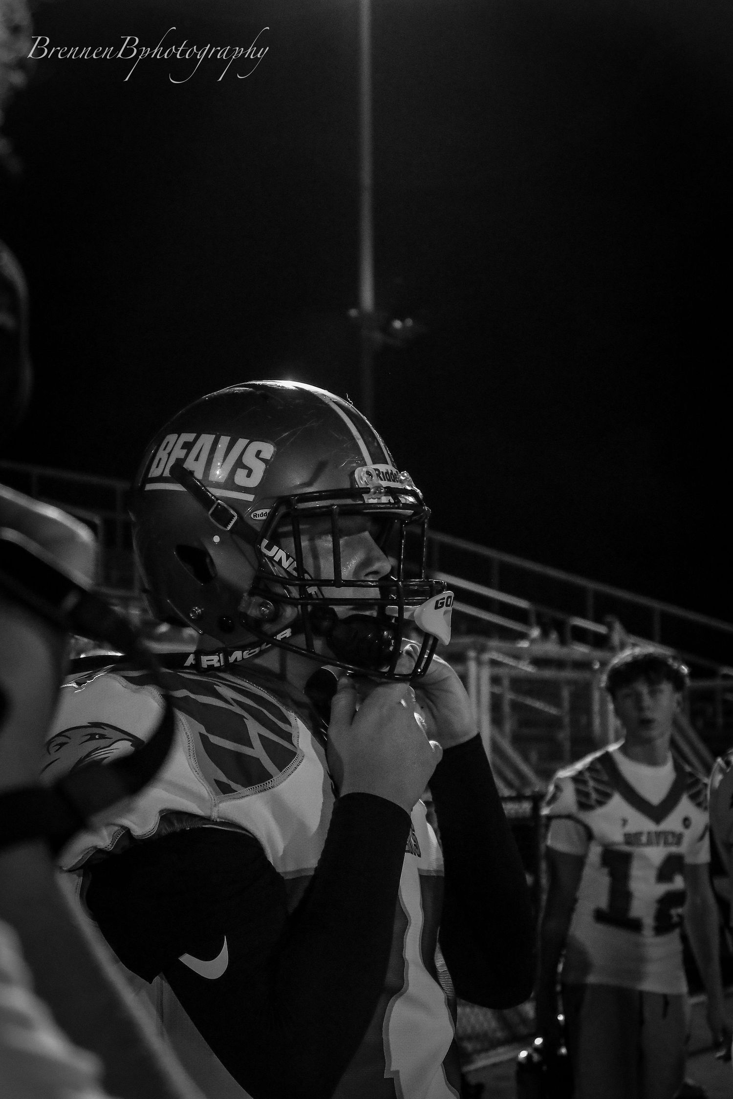 Black and white sideline photo of a Beavs football player adjusting his helmet during a night game.