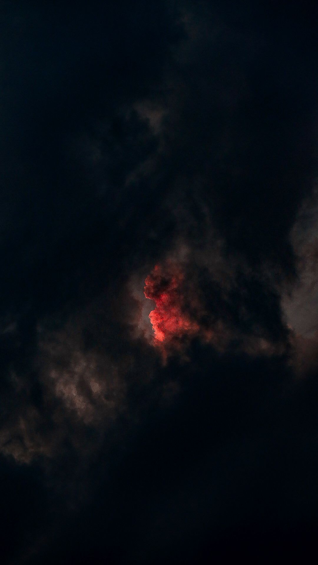 Dark stormy clouds with a glowing red light illuminating the center of an ominous night sky.