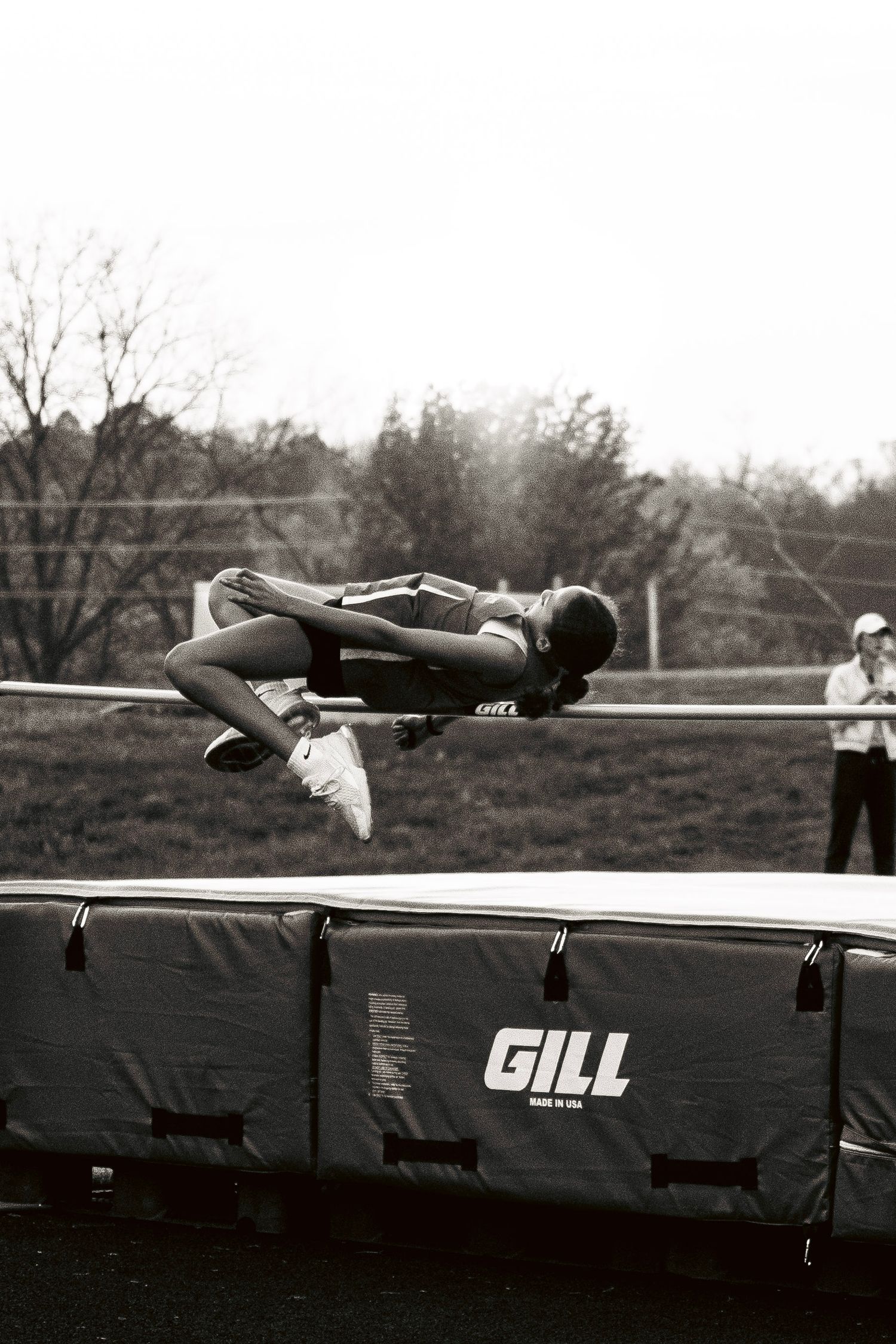 Black and white photo of an athlete performing a high jump over a Gill mat.