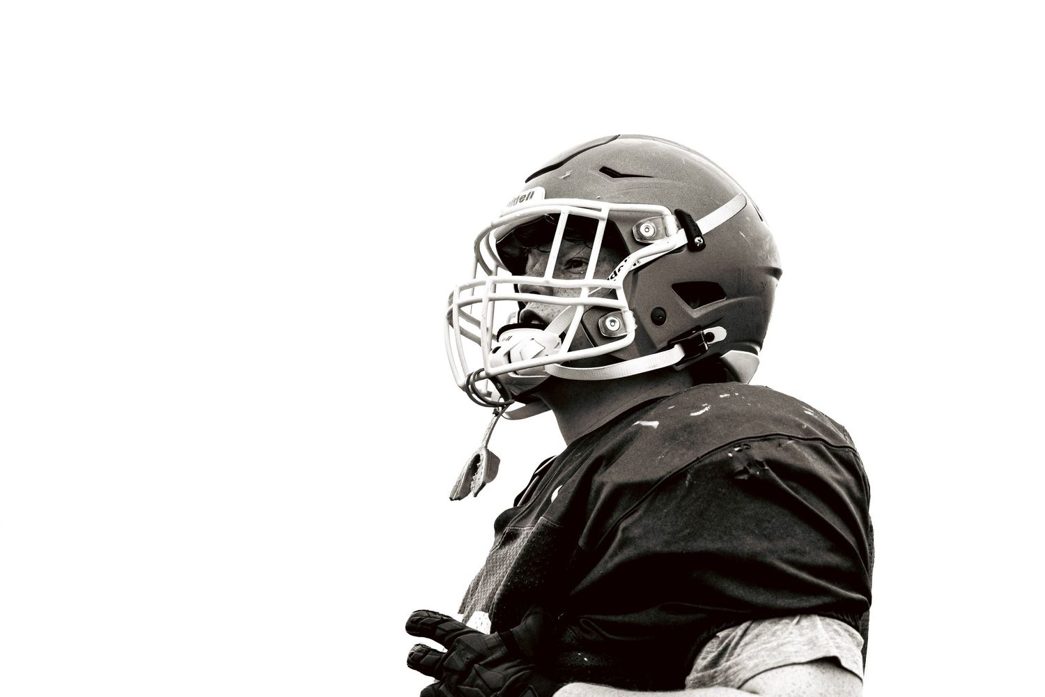 Black and white close-up profile portrait of football player wearing helmet and pads.