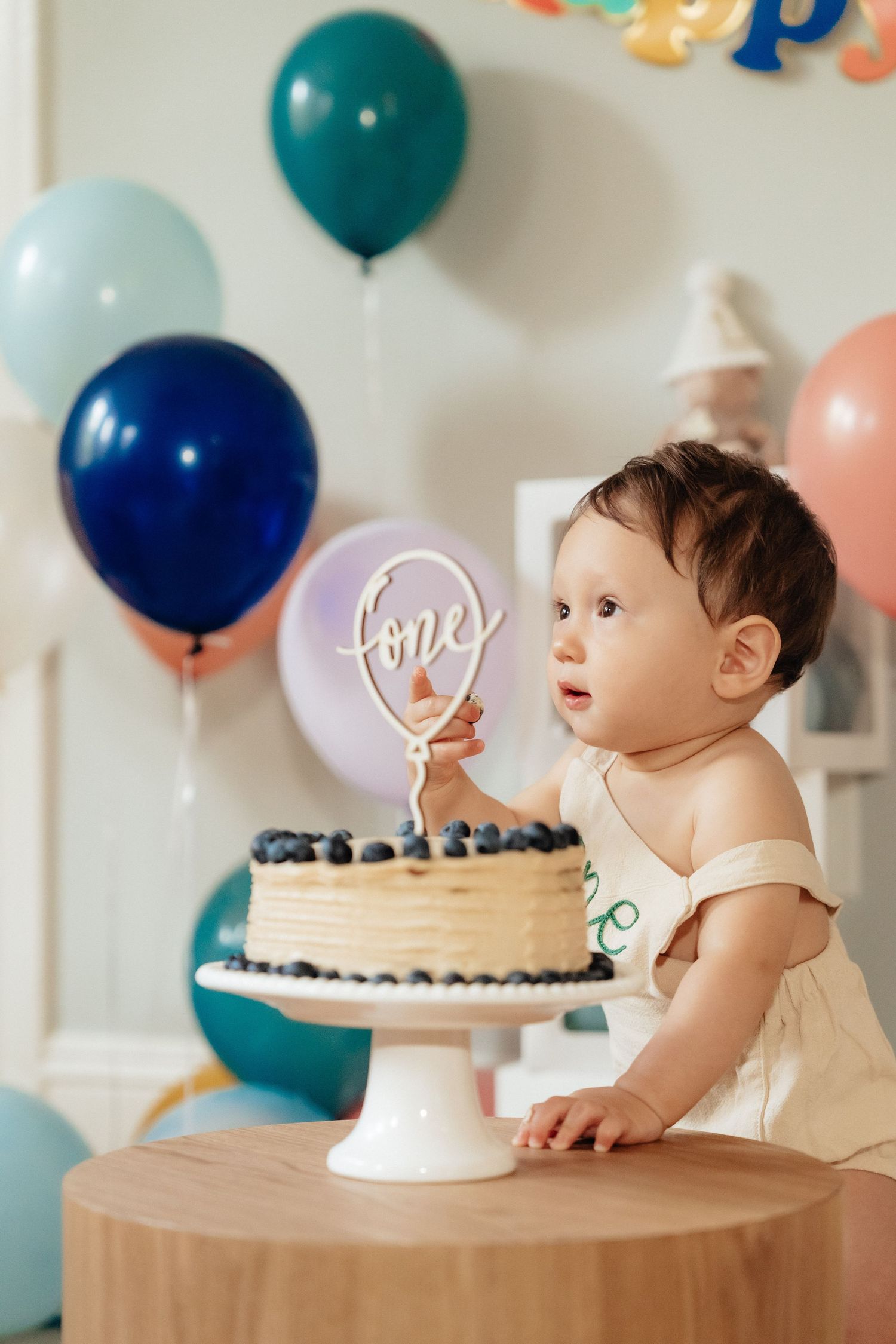 Baby's first birthday celebration with cake and colorful balloons in soft lighting.
