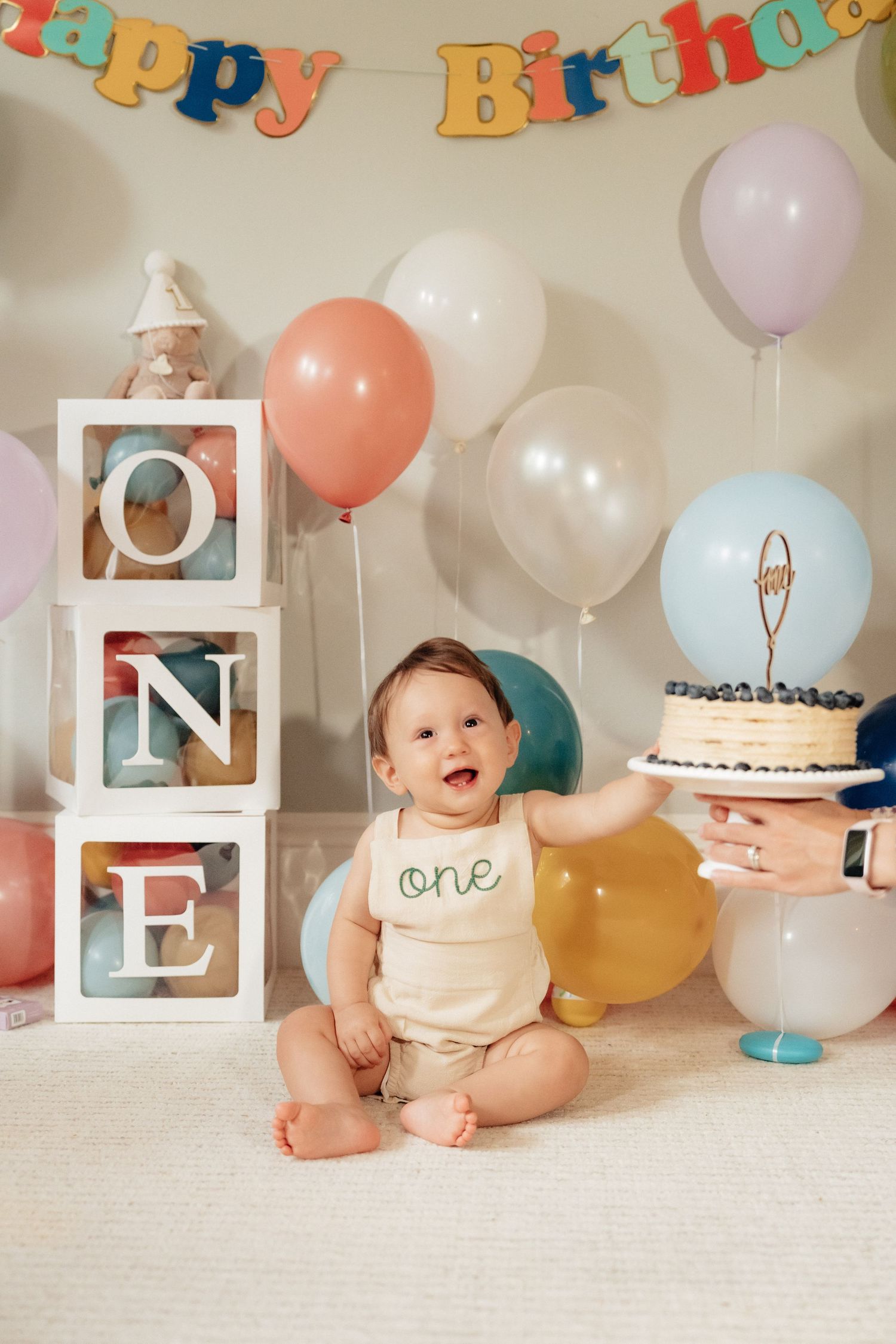 First birthday setup with decorative letters, balloons, and cake on wooden platforms.