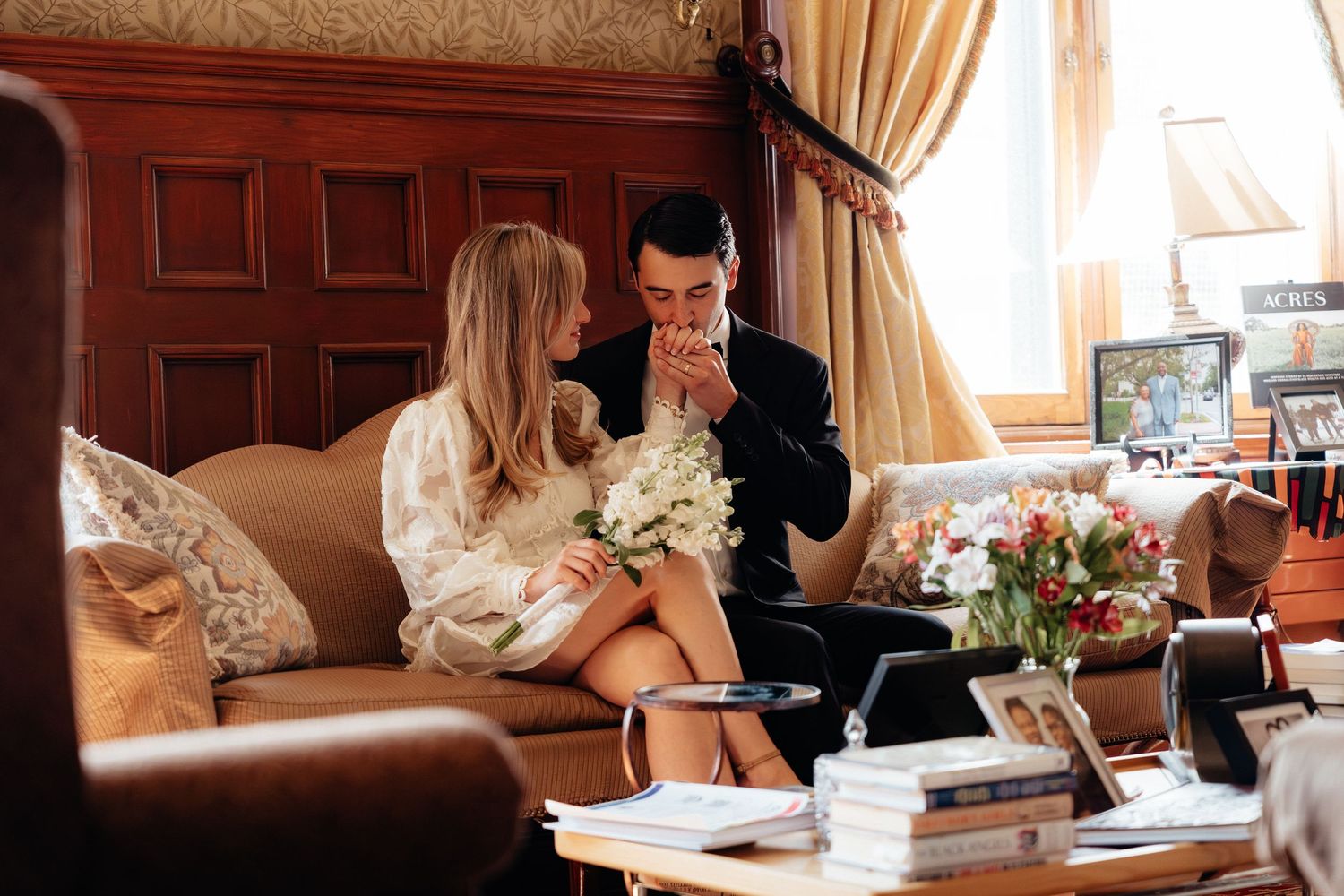 Intimate indoor photo session with white dress and dark suit against wooden paneled walls.