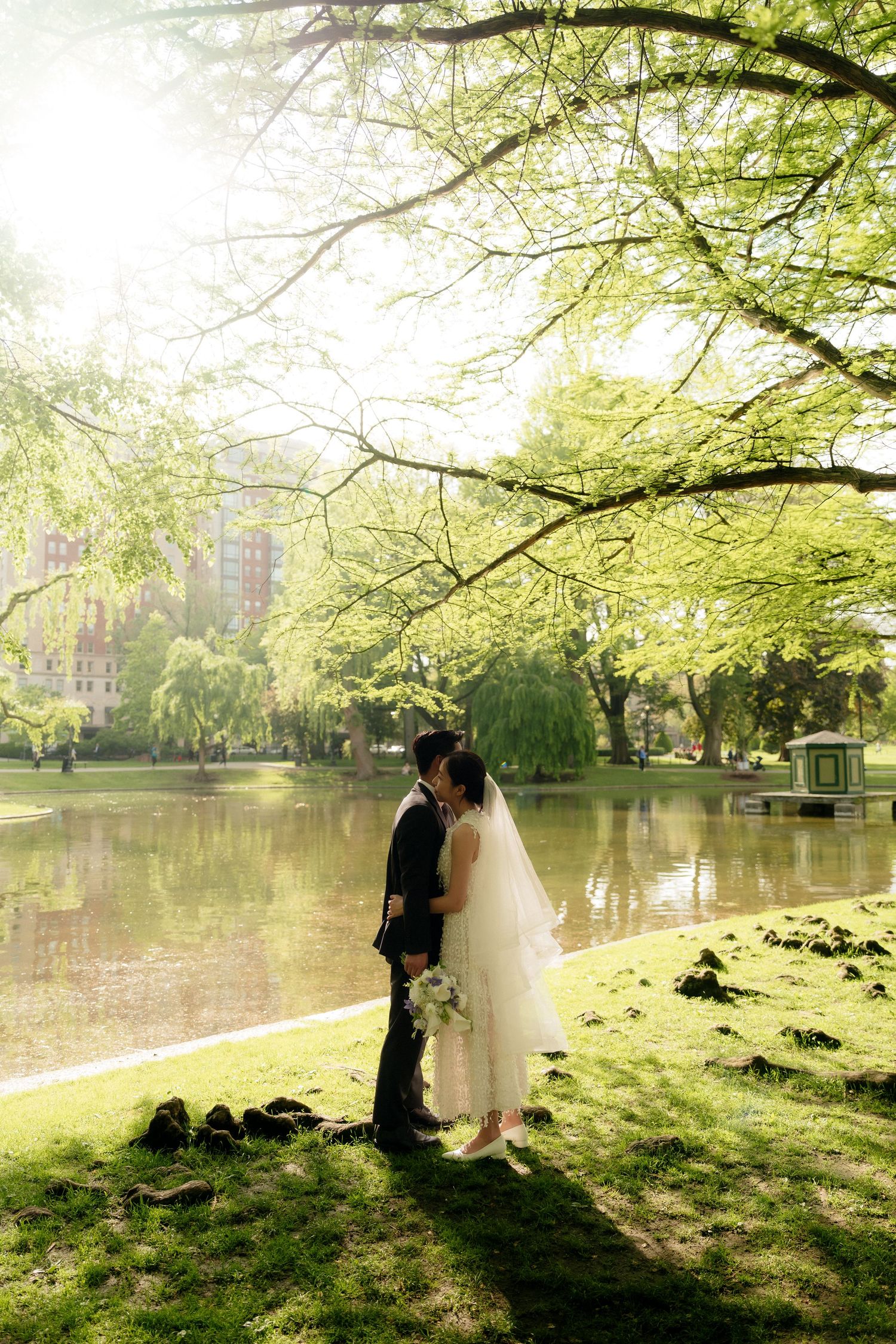A couple stands by a serene lake with overhanging trees creating a dreamy atmosphere.