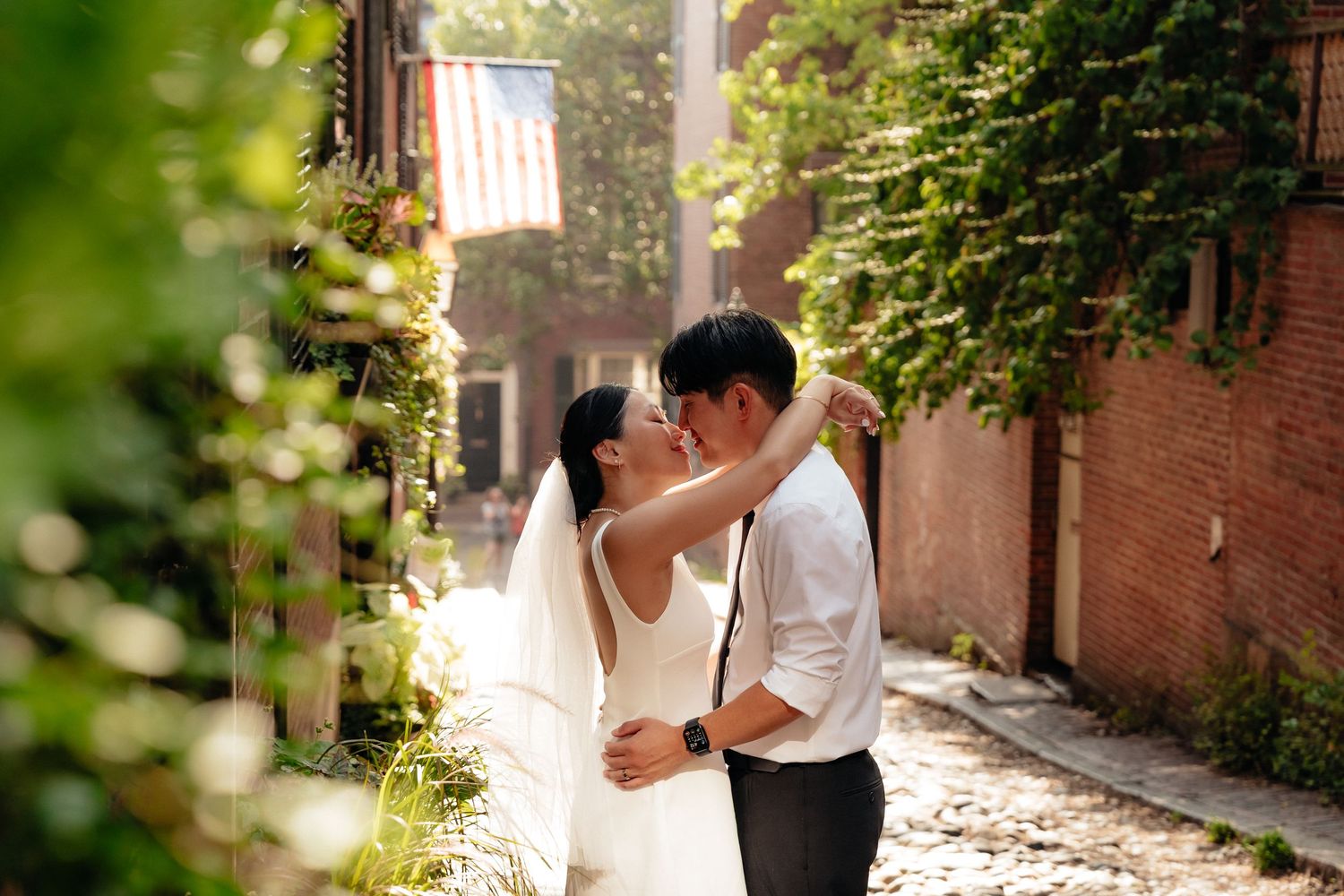 Couple embraces in romantic moment along ivy-covered brick wall pathway.