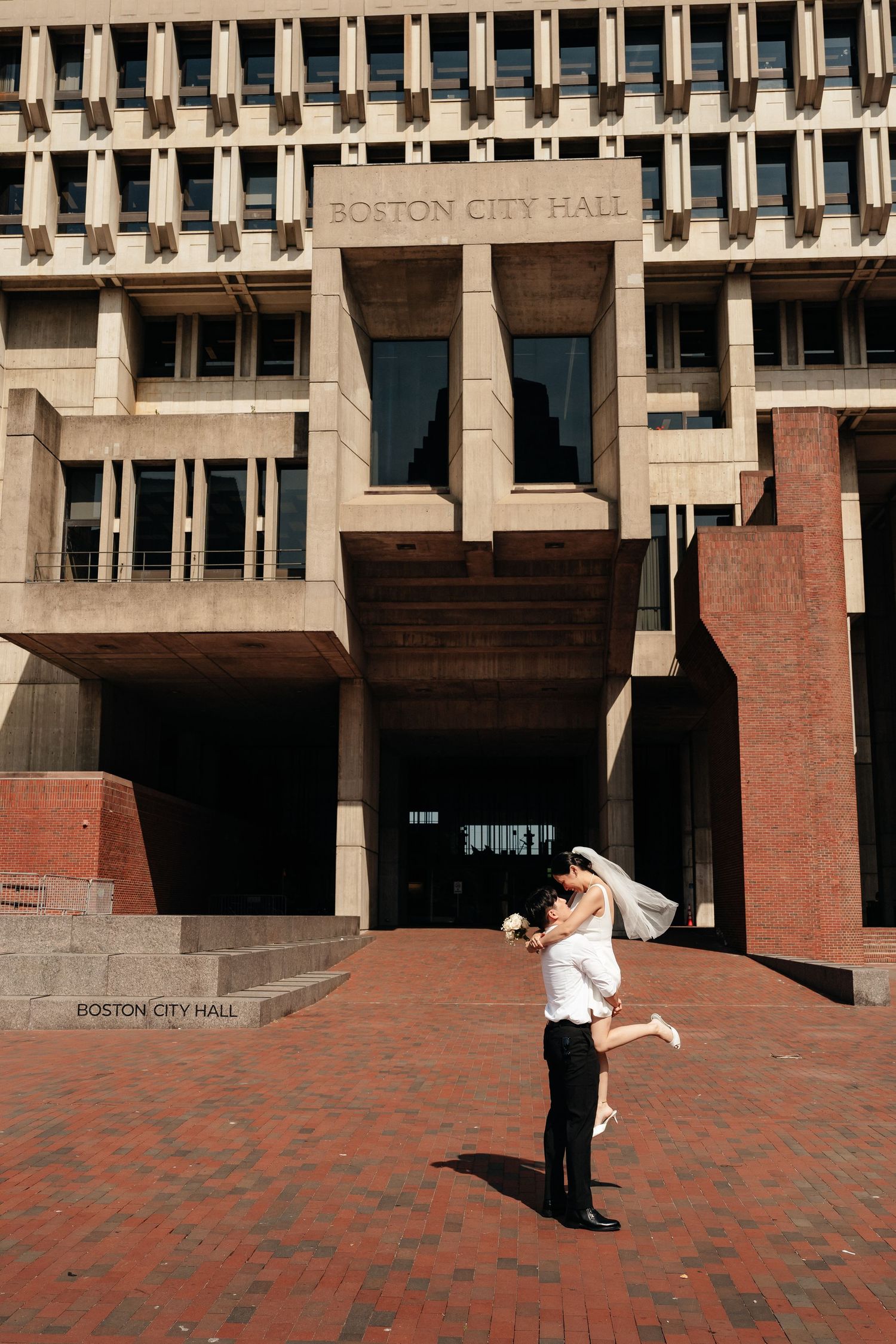 Couple poses playfully in front of Boston City Hall's brutalist architecture.