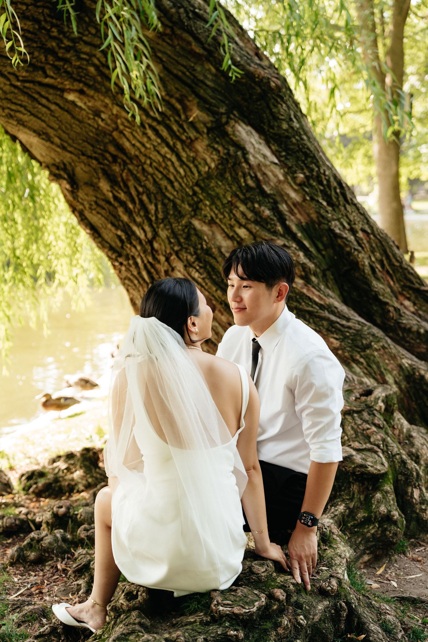 A couple shares a tender moment while sitting on a large tree trunk by a pond.