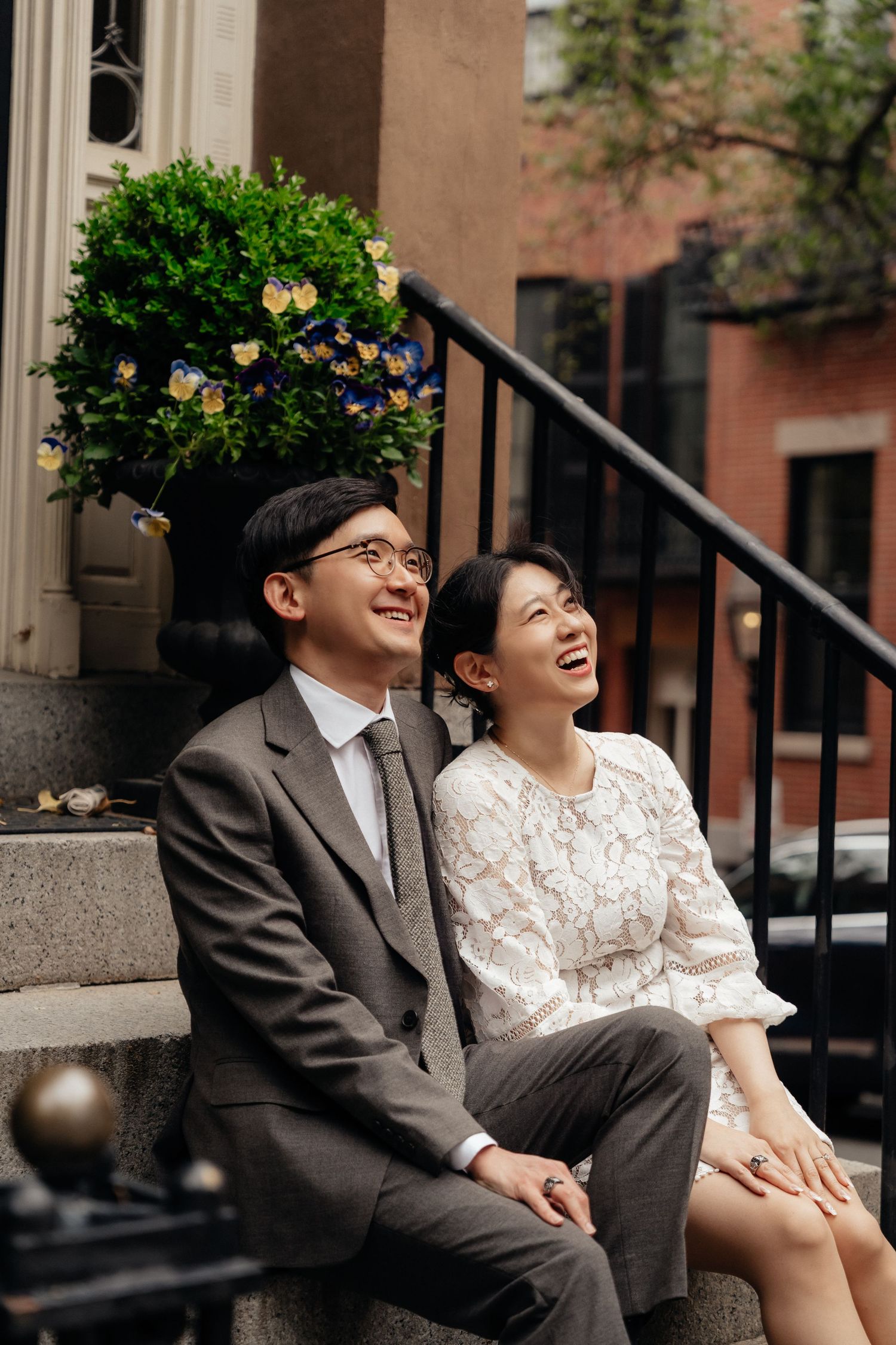 A couple shares laughter while sitting on stone steps outside a historic building.