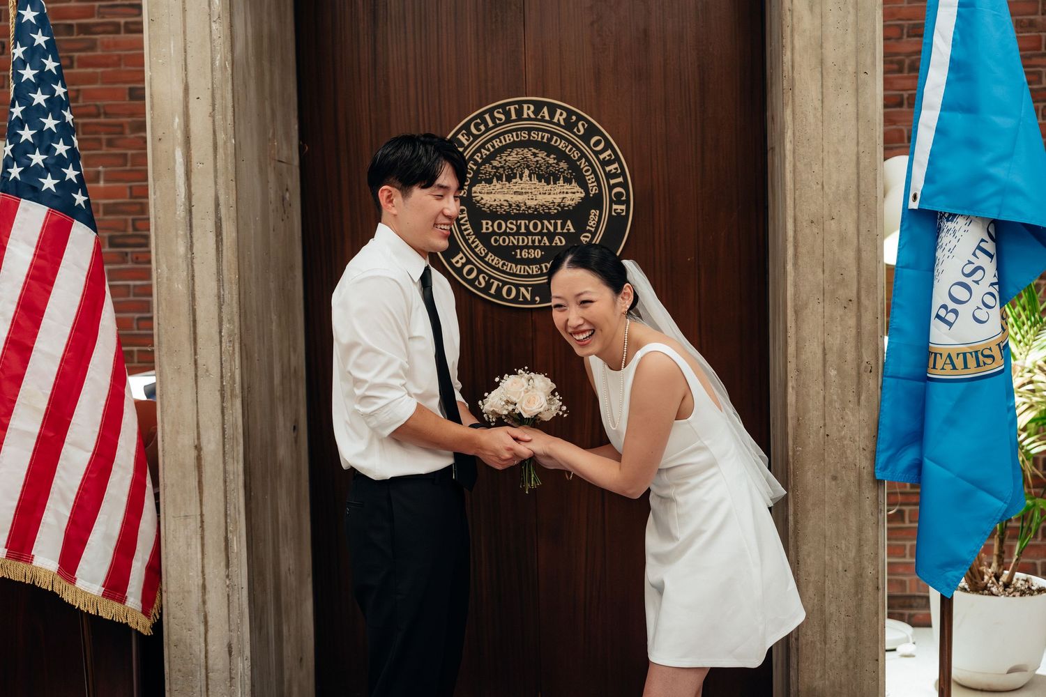 A couple in white and black formal attire share a romantic dance pose in front of American and state flags.