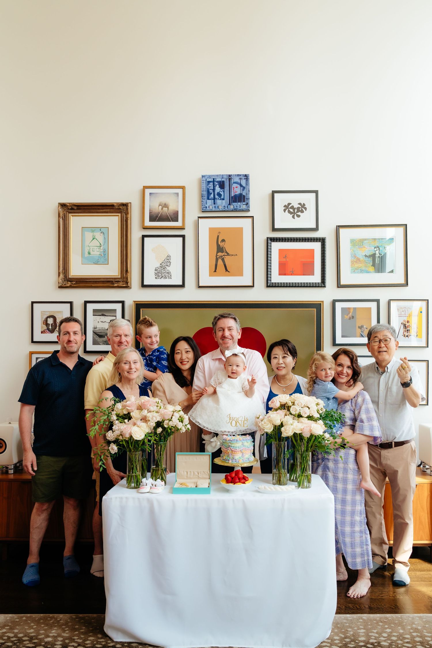 Group photo of party guests standing behind tables with floral arrangements and framed artwork on walls.